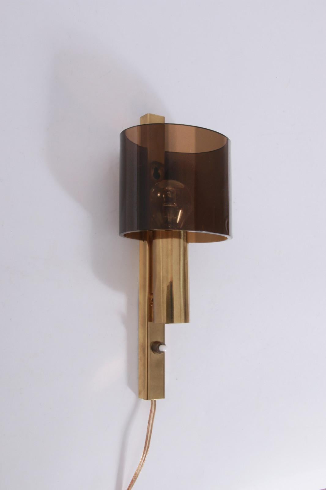 

Questa elegante applique, progettata e prodotta da Hassel & Teudt in Danimarca a metà degli anni '60, presenta una struttura in ottone dorato che sostiene un paralume ovale in vetro acrilico fumé. 
Combinando l'elegante design danese con materiali
