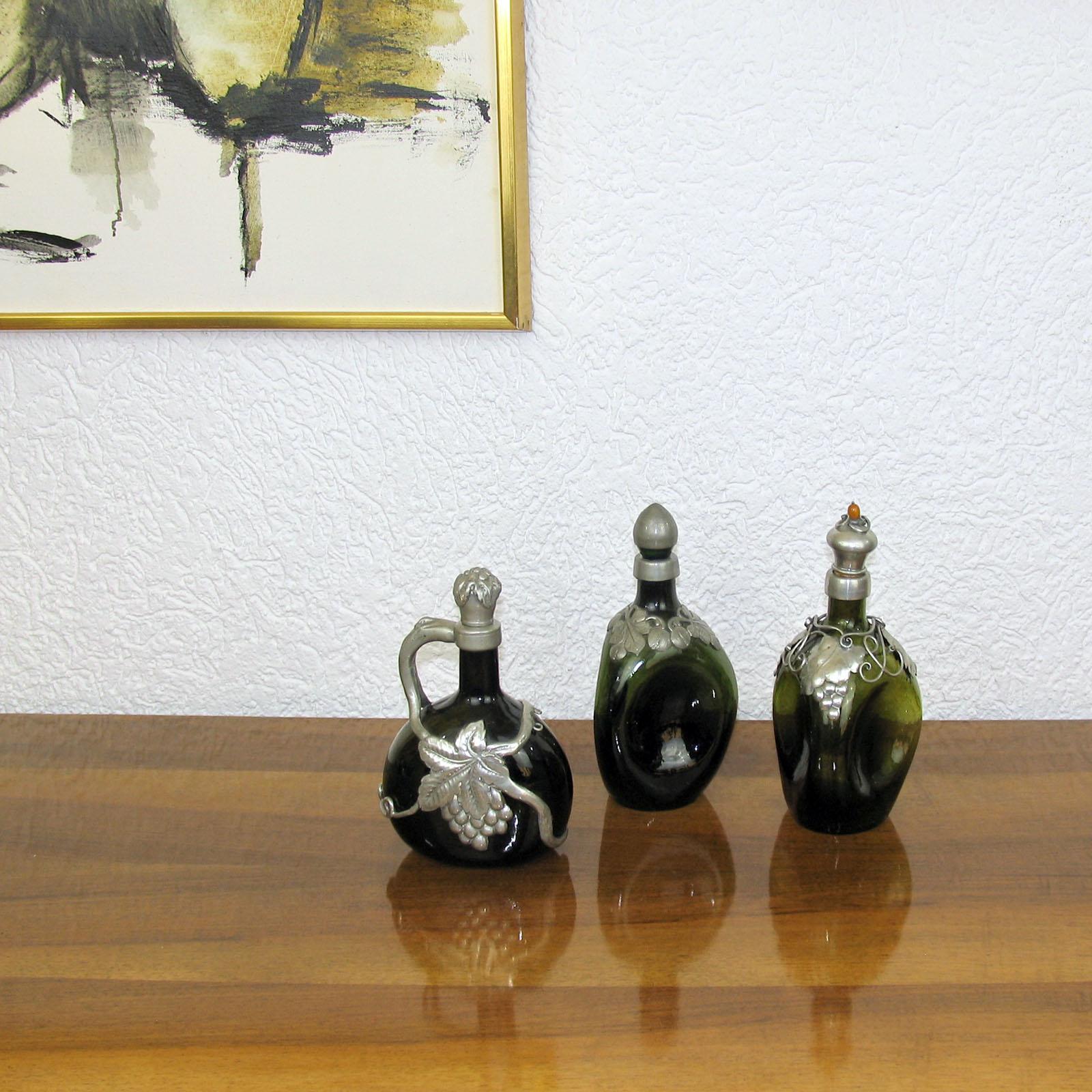 Triangular dark green glass bottle with pinched sides, embossed pewter overlay and stopper. Very good used condition. After a design of Georg Nilsson. 
Measure: Height 24 cm.