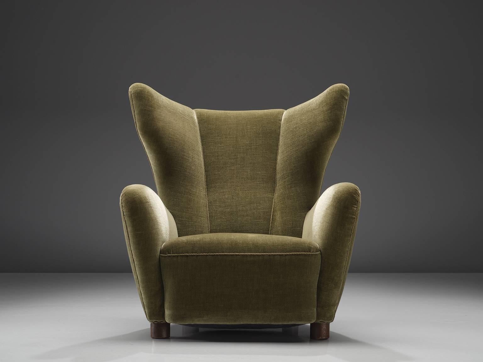 Danish cabinetmaker, wingback chair, mahogany, green velvet fabric, Denmark, circa 1940

This easy chair has a grand wing and a sectioned back. The seat is thick and the armrests are thick, full and rounded. The sides are smooth and soft and the