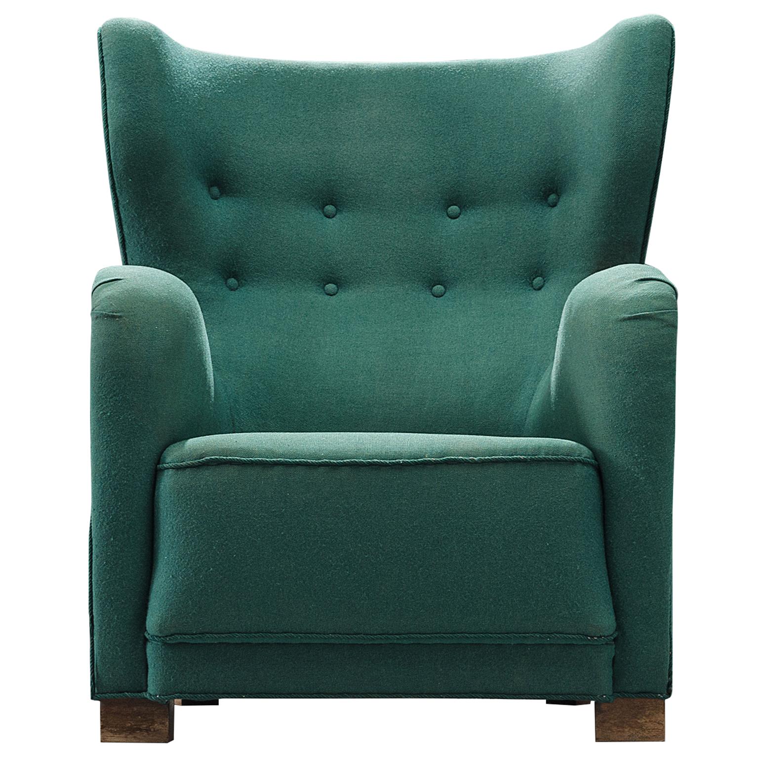 Wingback lounge chair, made with green wool and wooden blocks, Denmark, 1940s. 

The chair has a high wingback which features green upholstery with two rows of buttons on the top and sturdy block wooden legs. When seen from the front the chairs