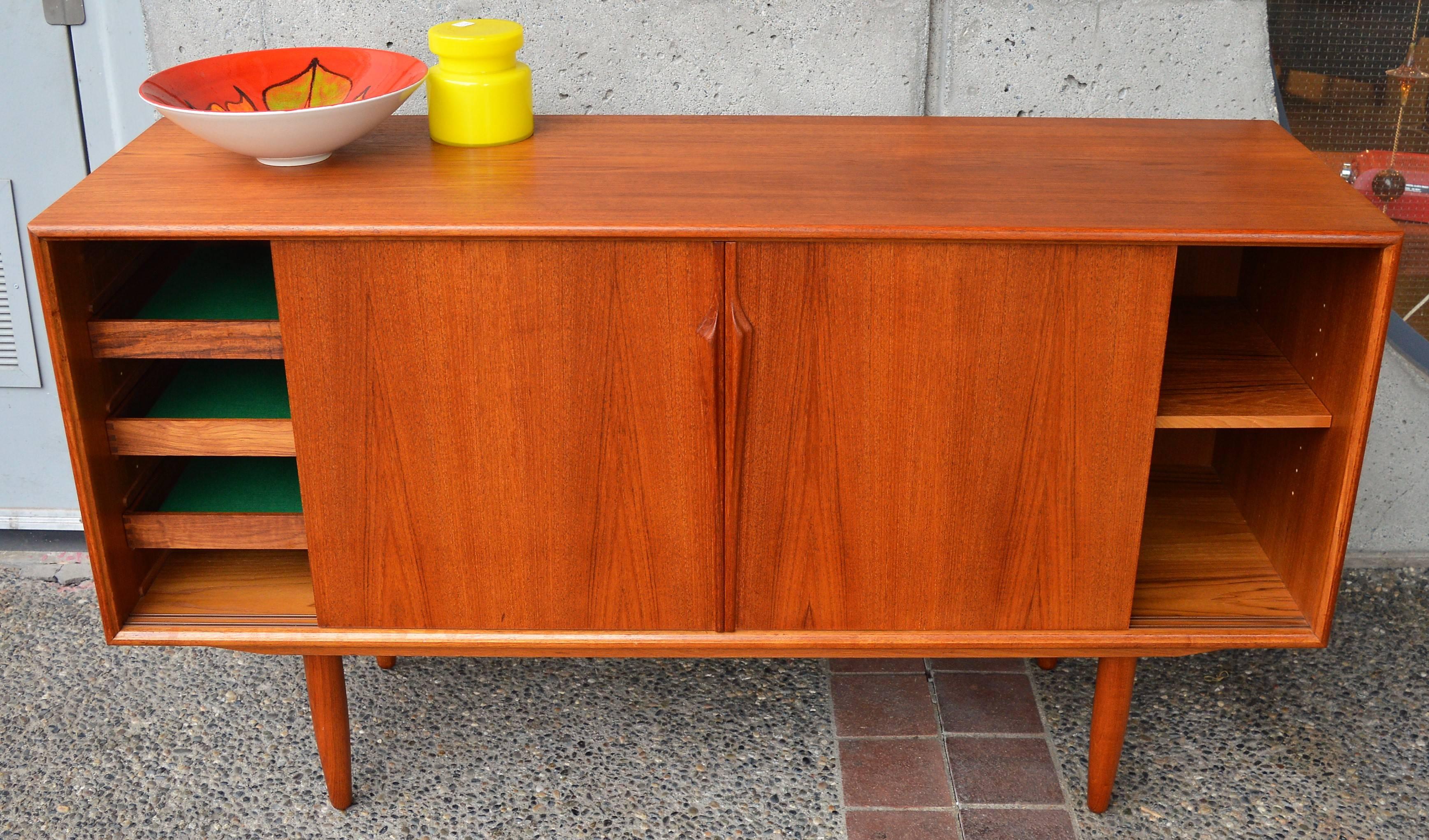 This stunning Danish Modern teak mid-sized credenza / buffet was designed by Gunni Oman for Axel Christensen in the 1960s. I adore the intricately carved door pulls! Featuring a lovely wood tone, with book marked veneers on the doors. The interior
