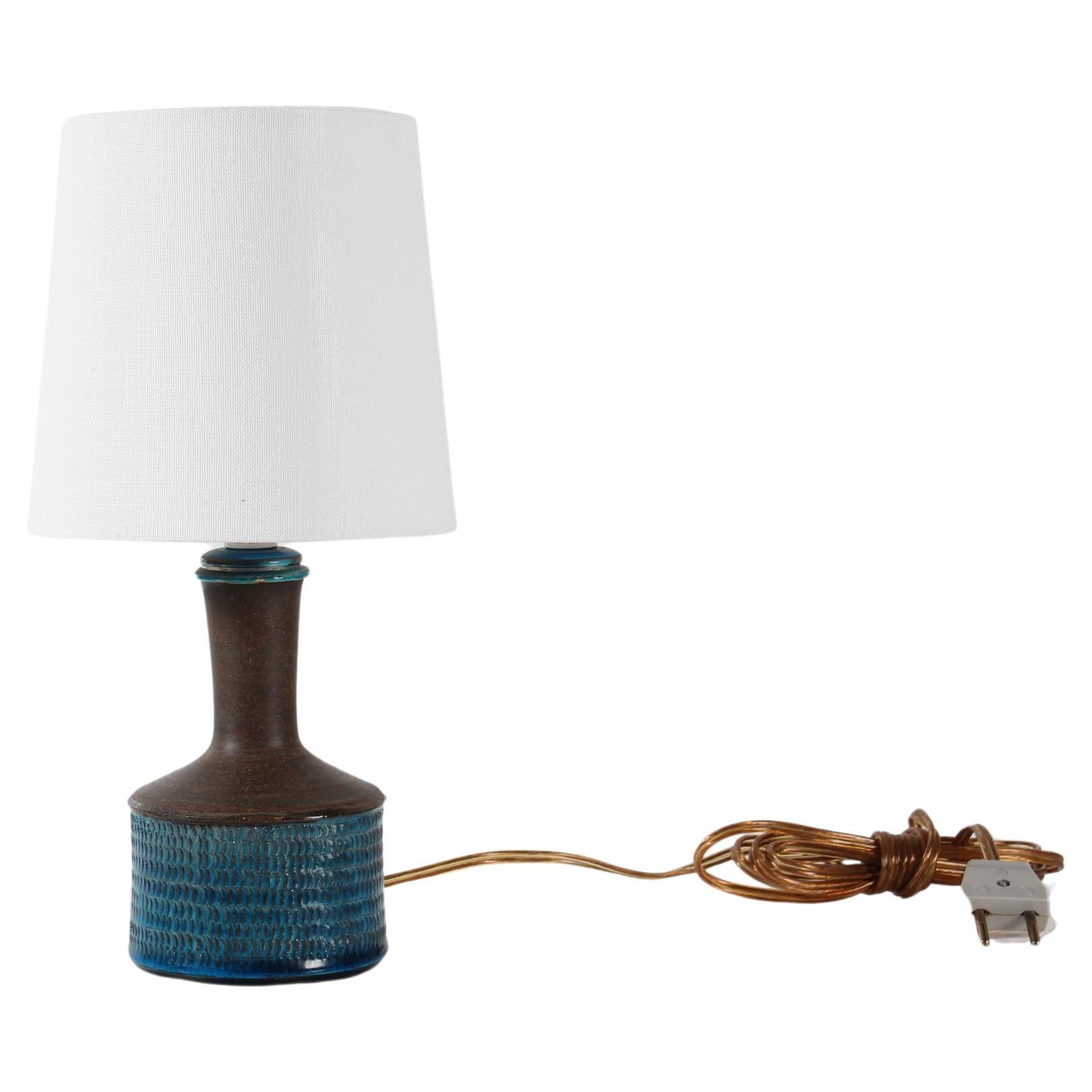 Small mid-century Danish table- and bedside lamp.
it's designed by Nils Kähler for the ceramic workshop Kähler (HAK) in Denmark in the 1970s

It's decorated with a glossy turquoise blue glaze on a structured surface. The neck is smooth and