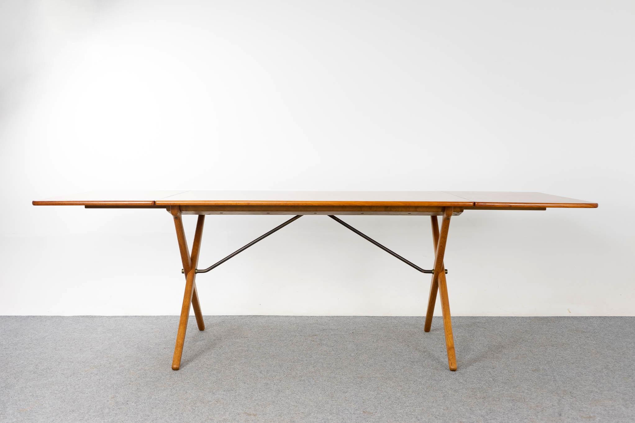 Teak and oak Danish AT-309 dining table by Hans Wegner, produced by Andreas Tuck, circa 1950's. Stunning drop leaf table with unique cross legged solid oak base with elegant brass support detailing. Table top shows minor veneer wear, expertly