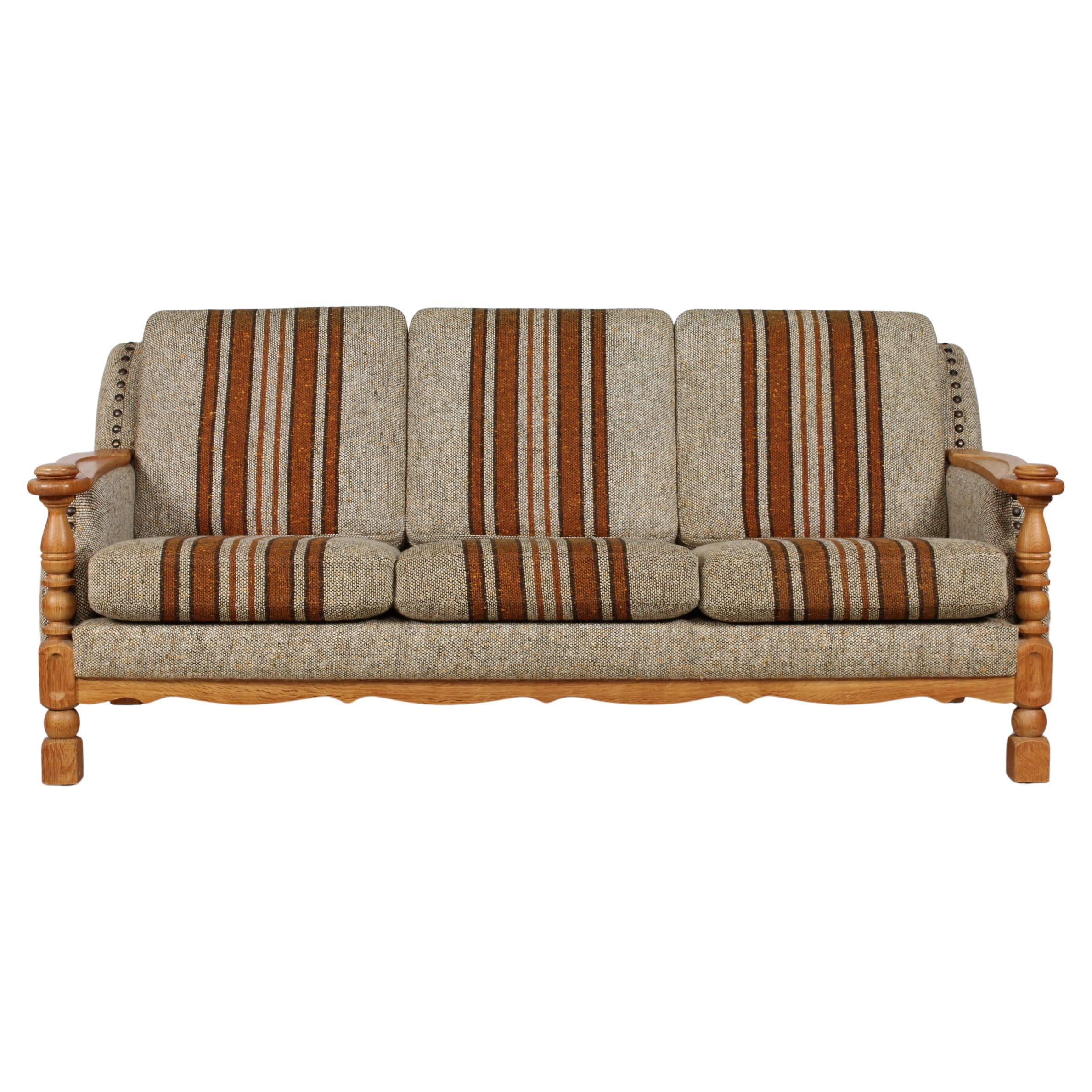 Danish vintage sofa most likely designed by Henning Kjærnulf and manufactured in Denmark by EG Møbler.
The frame and armrests are made of turned and carved solid oak upholstered with the original striped wool with brass nails. 

A great sofa in the