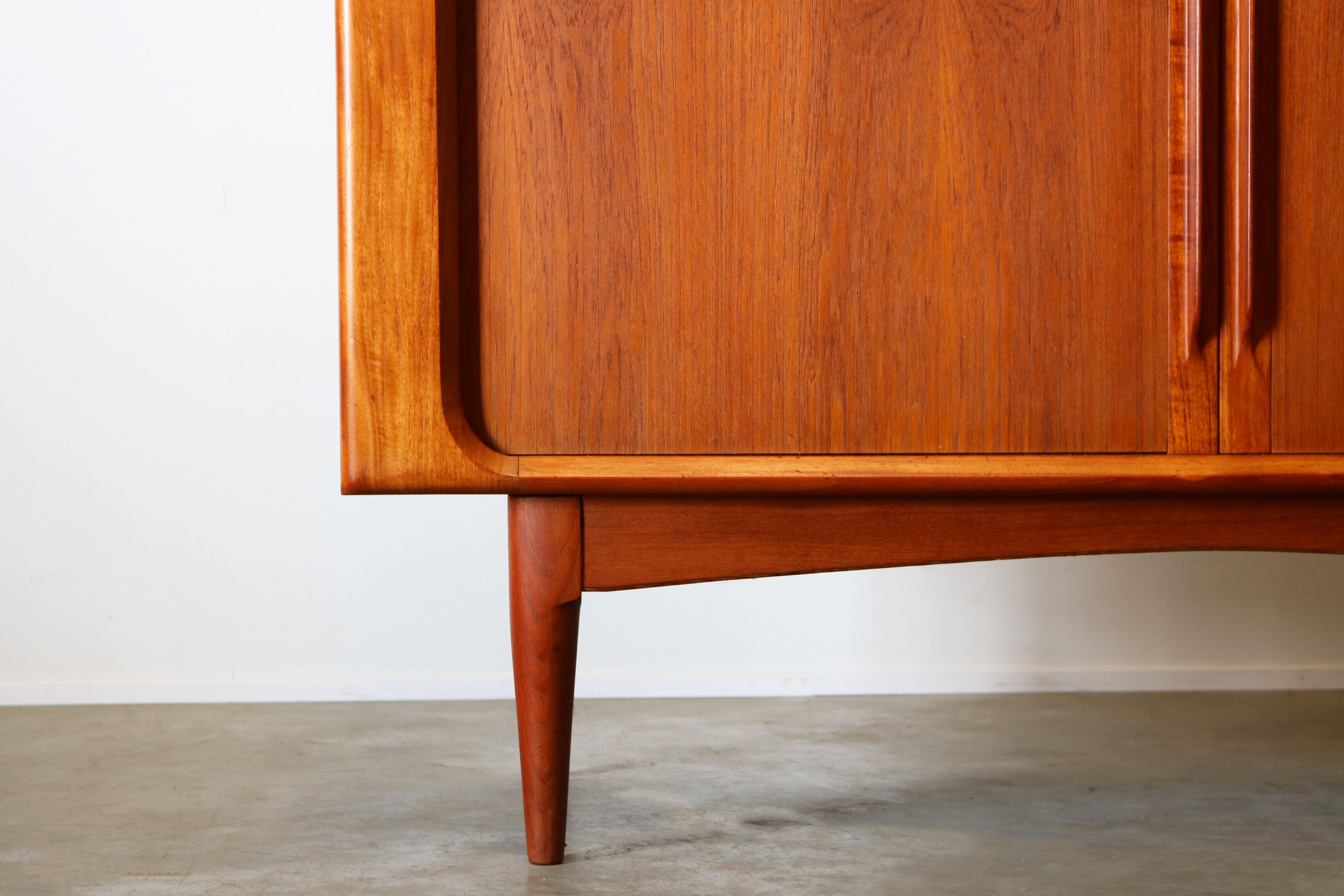 Magnificent Danish design highboard designed by Bernhard Pedersen & Son in the 1950s. The highboard is made from solid teak wood and its tambour doors disappear completely when opened. The highboard has three drawers and multiple shelves that