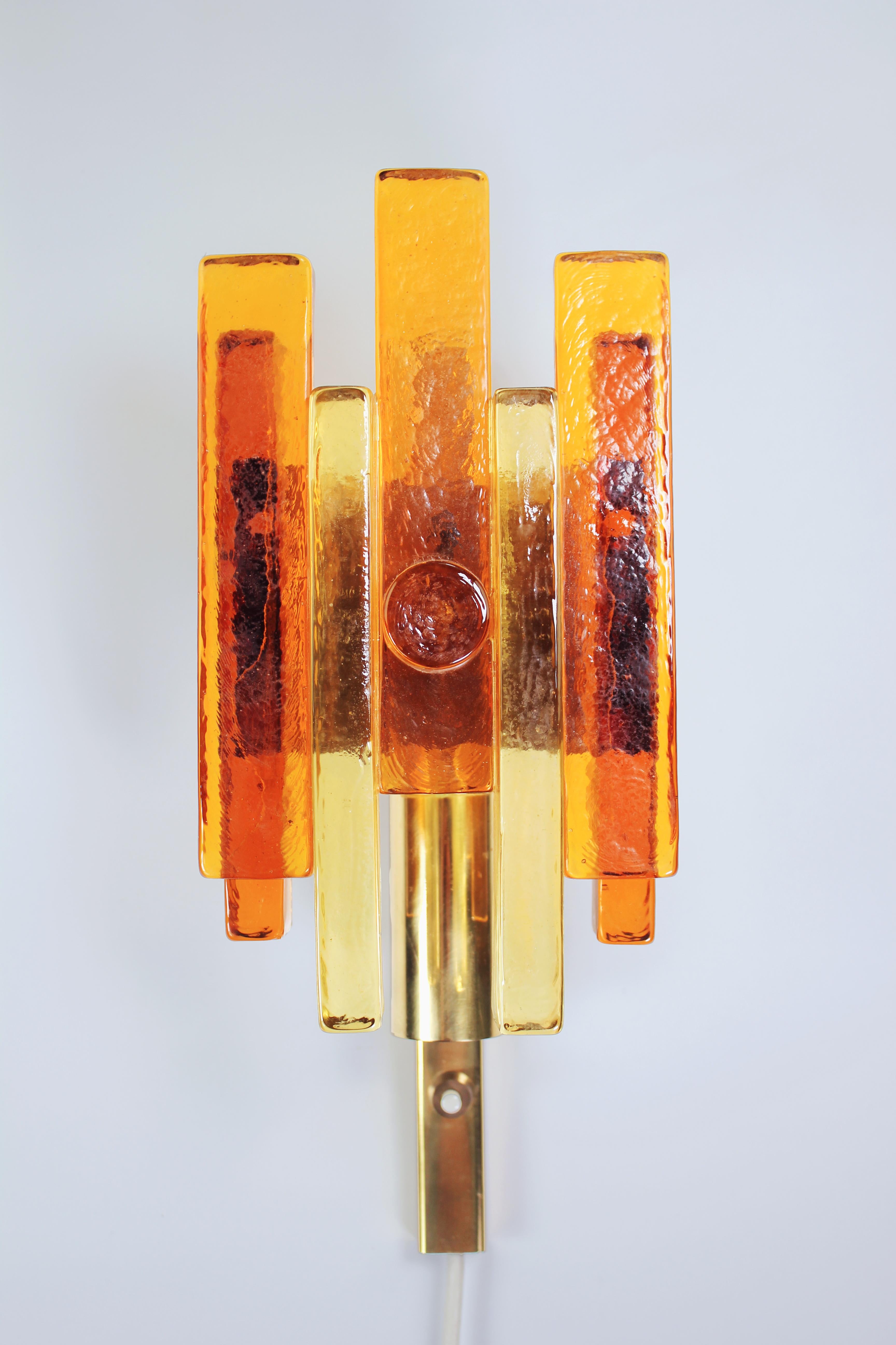 Danish modern tinted solid glass wall light by Svend Aage Holm Sørensen for Hassel & Teudt. Solid and heavy amber and yellow golden glass sticks stacked in symmetrical pattern with a circle in the center, all on polished golden metal mount. Designed