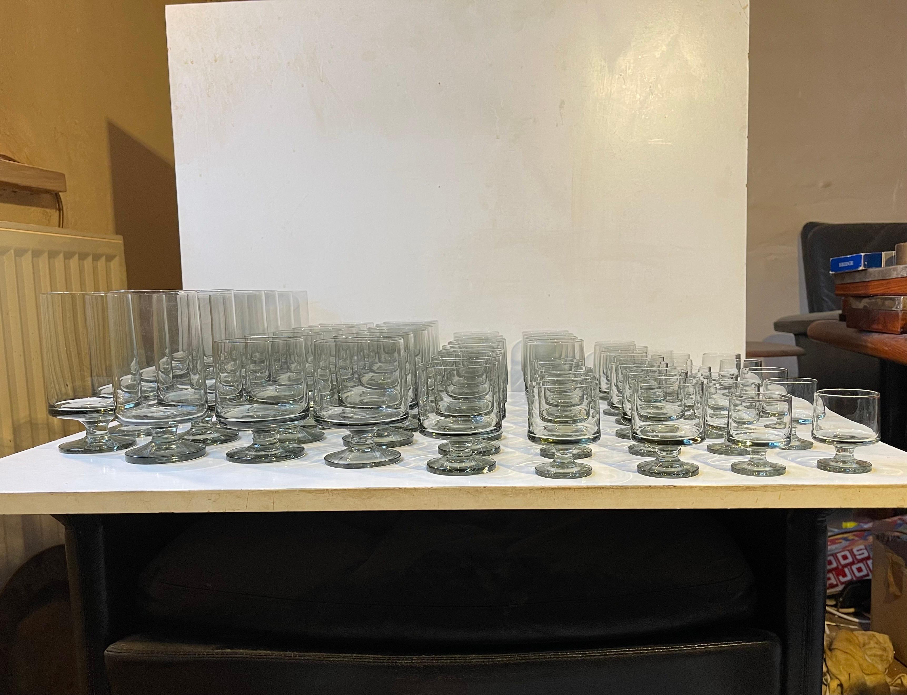 Extensive set of barely used and NOS drinking glasses in a distinct smoke grey tone. Designed in 1958 by the female designer duo Grethe Meyer and Ibi Trier Mørch. Most of the pieces particular the larger ones are hand-signed underneath the bases.
