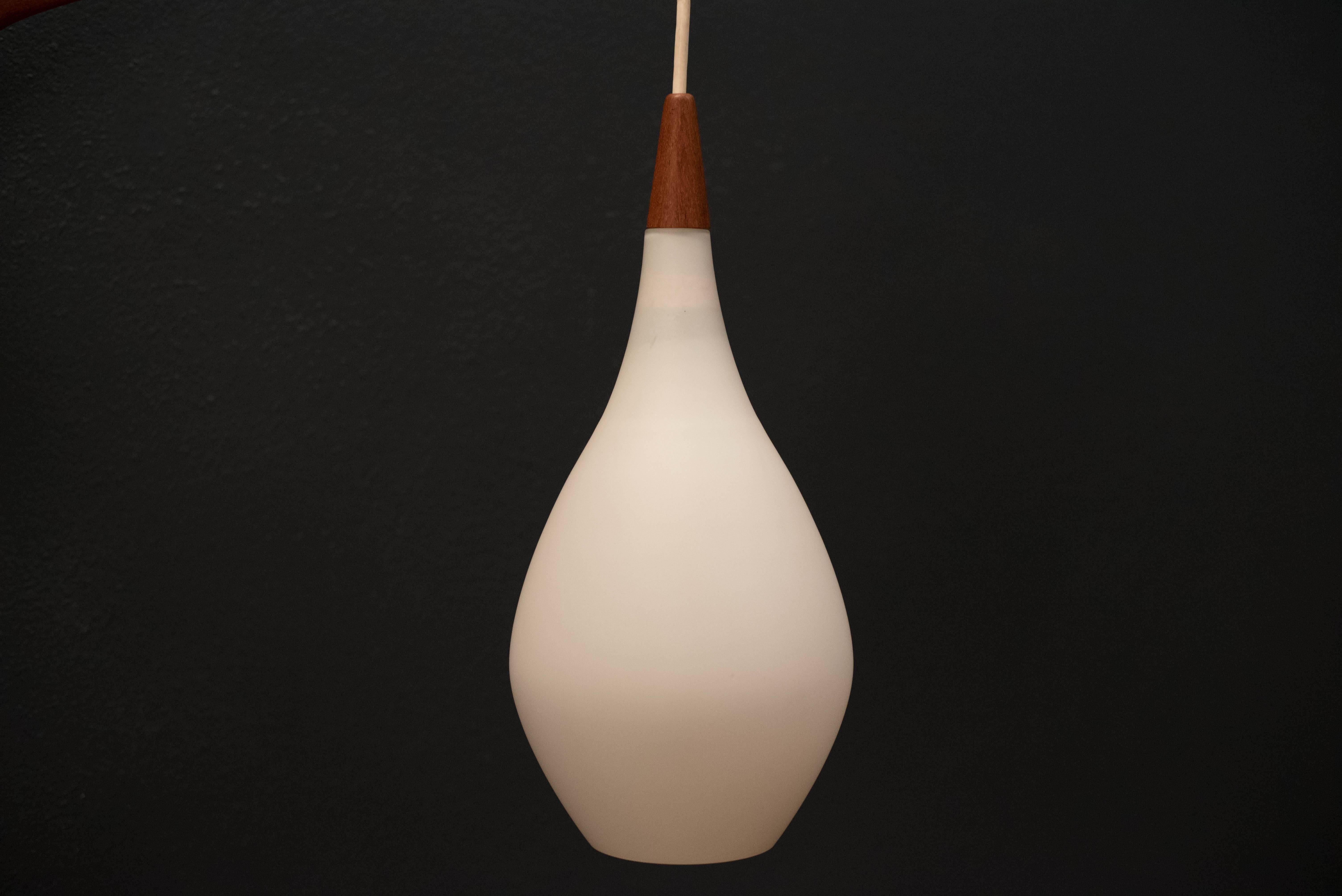 Mid-Century Modern hanging wall light by Holmegaard in teak. This piece displays a white frosted glass shade and includes a teak swing arm with adjustable cord. 

Swing arm: 23.25