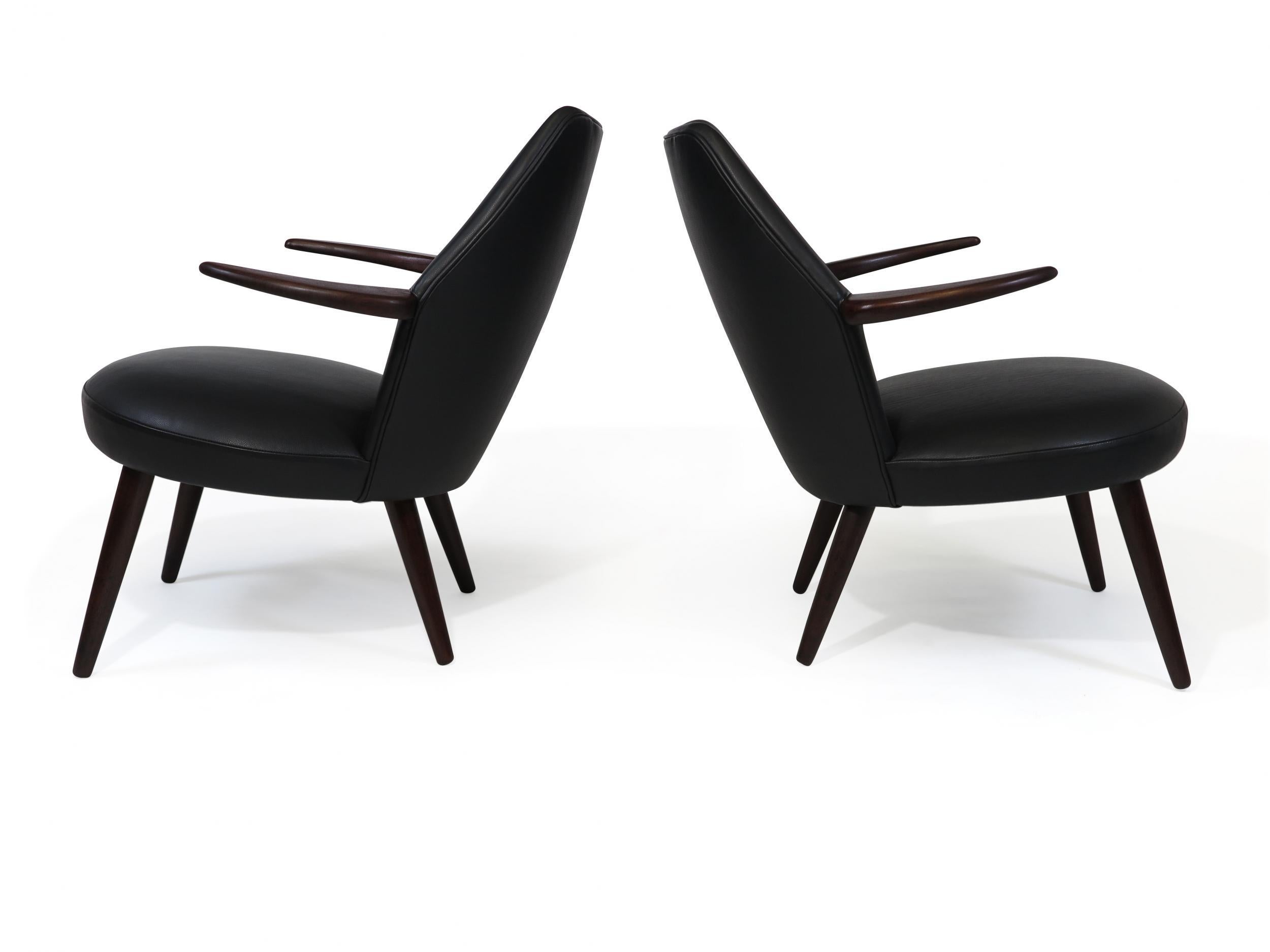 Midcentury Danish lounge chairs with curved back and horn shaped arms, raised on tapered teak legs, newly upholstered in black leather.