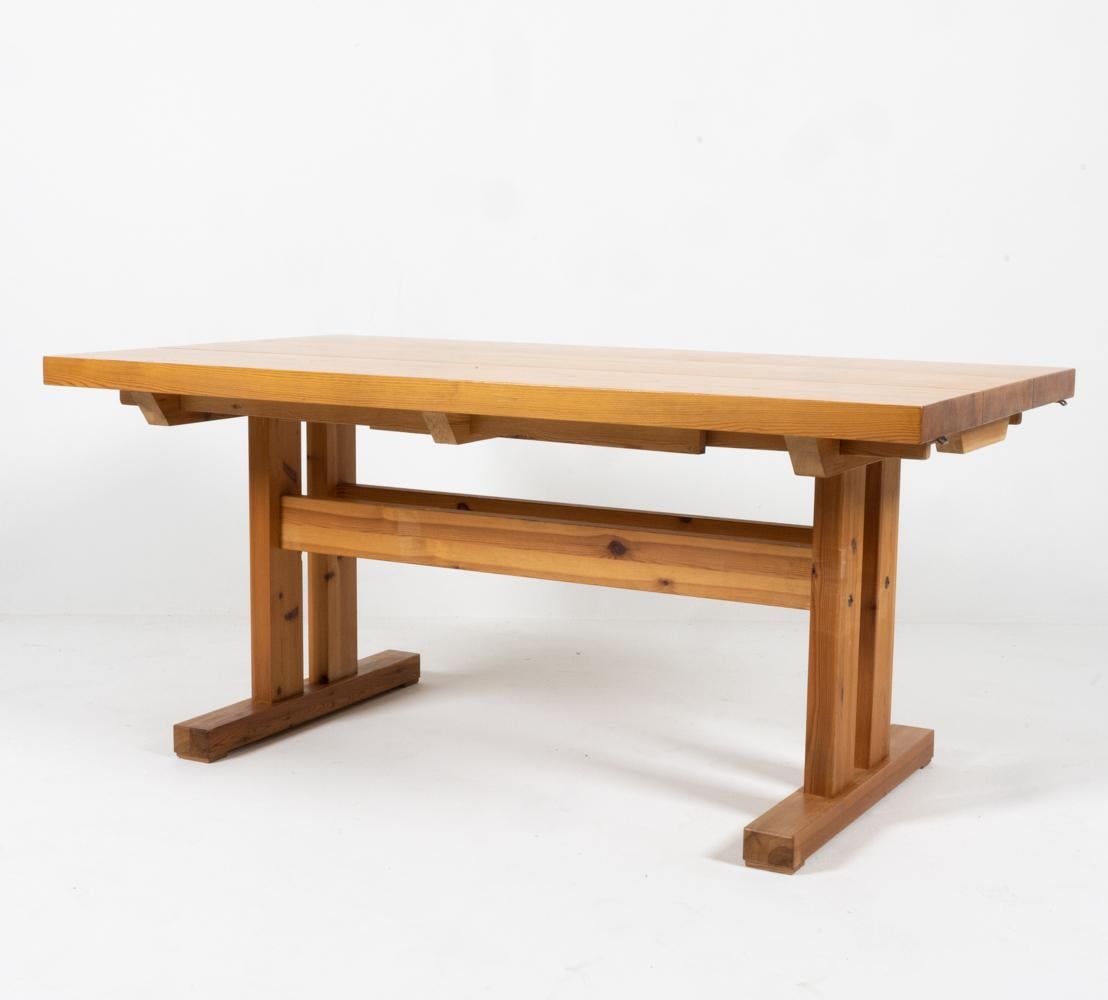 Exuding rustic warmth with a brutalist modern twist, this versatile pine dining table boasts a sturdy double stretcher with a trestle base. Two removable extension leaves attach with brass hinges to either end of the table, transforming this table