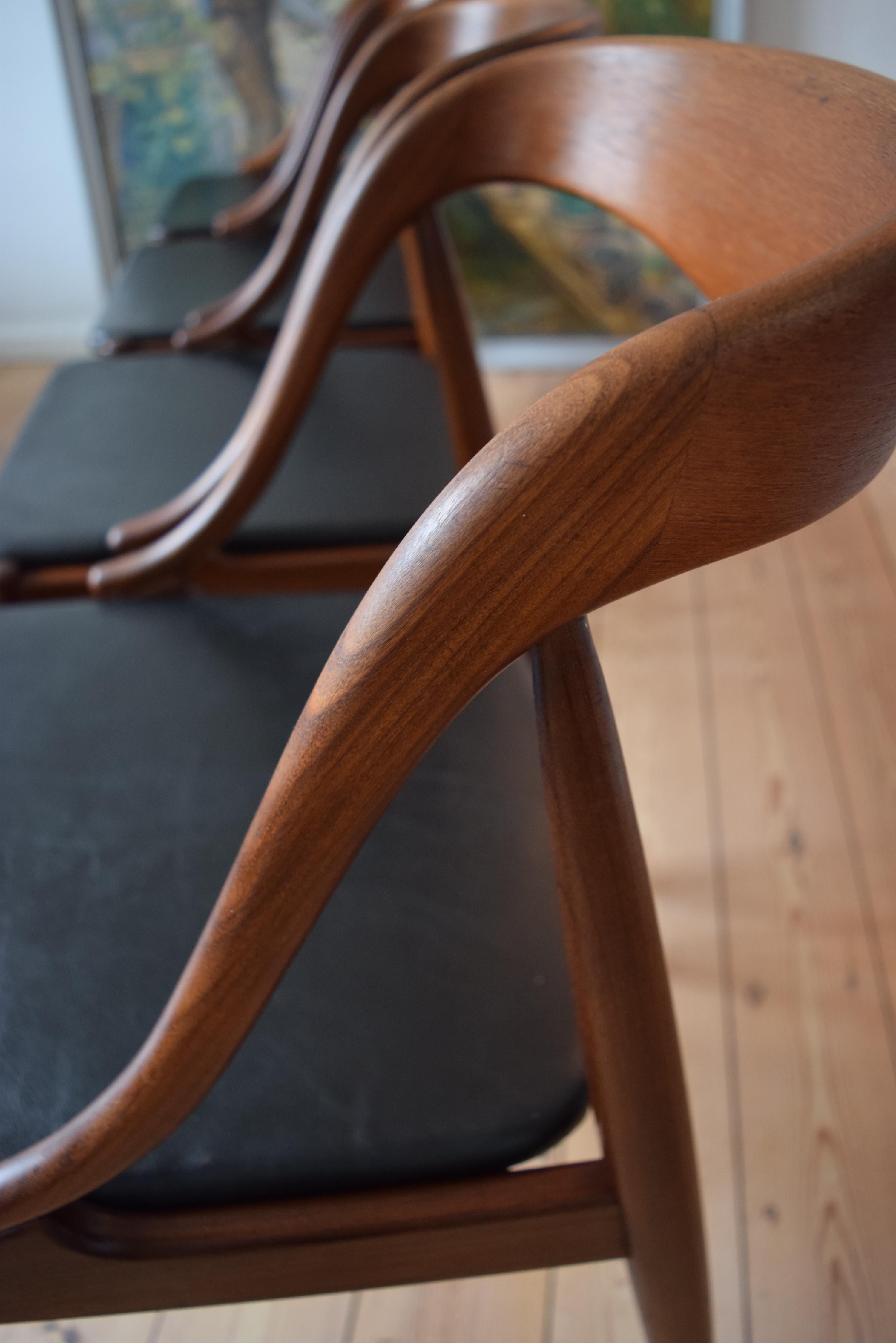 Set of four teak dining chairs by Johannes Andersen for Uldum Møbelfabrik Denmark, manufactured in the 1950s-1960s. The frame is made of teak and the seats are covered in black leather. This model features a deep curved backrest for extra comfort.