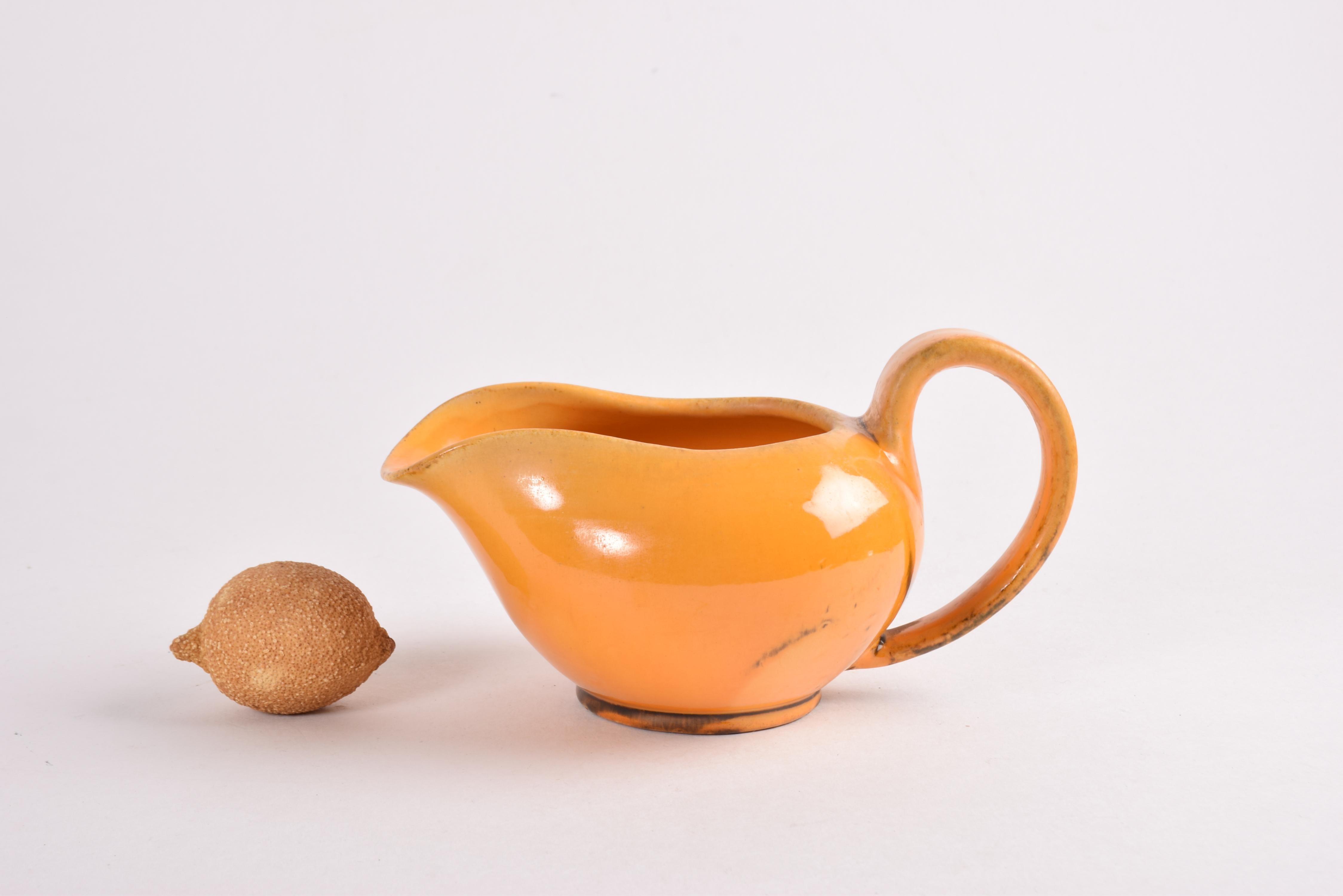 Pichet ou cruche en céramique Art déco conçu par Nils Kähler et fabriqué par l'atelier de céramique Herman A. Kähler dans les années 1930 ou 1940.
La cruche est décorée d'une glaçure jaune uranium chaude avec des éléments bruns. 

Signé sous le bas