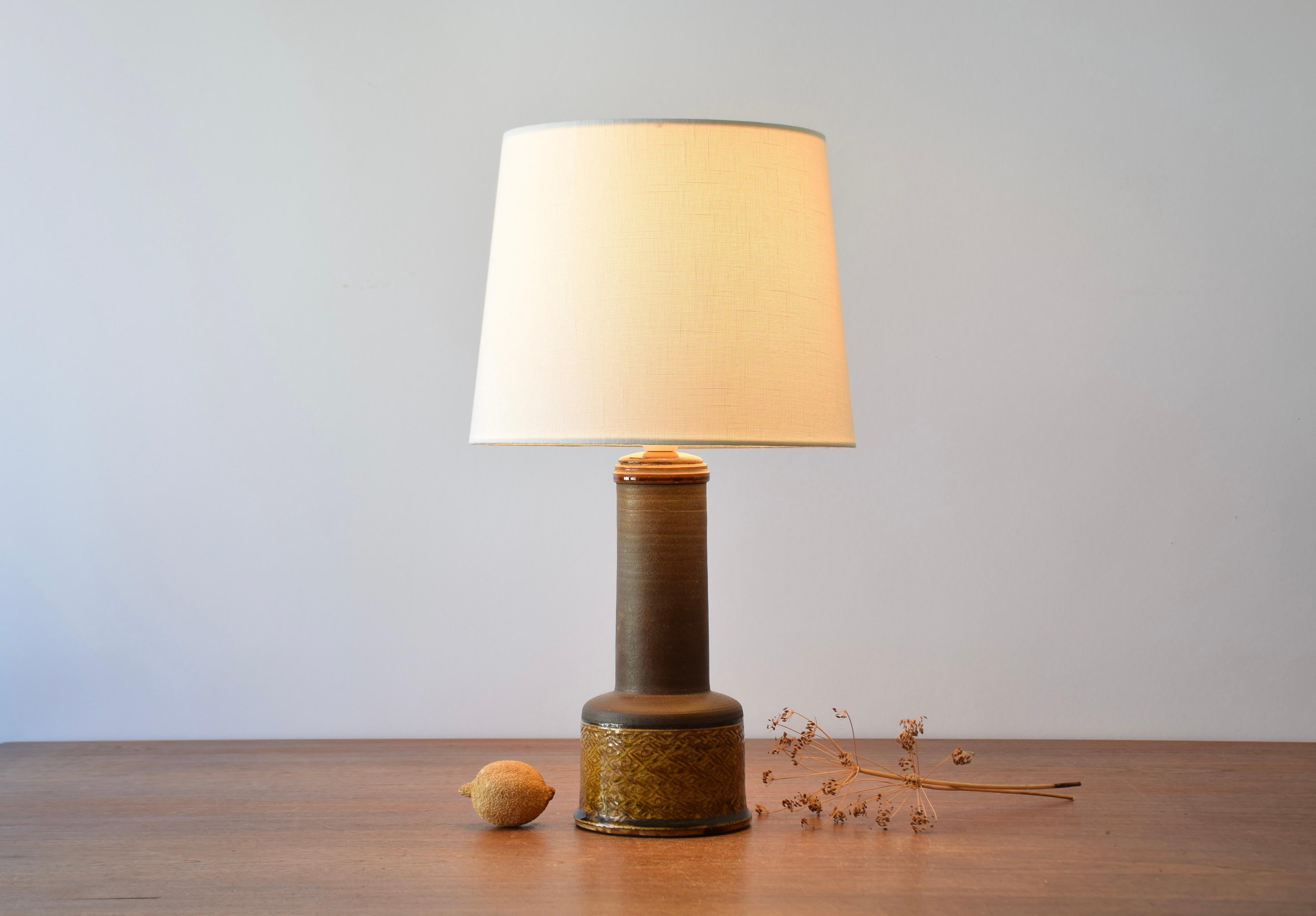 Table lamp from Herman August Kähler's ceramic workshop in Denmark. Made ca 1960s. The design is attributed to Nils Kähler.

The lamp base has an incised pattern and the glossy glaze is amber / curry colored. The neck and the shoulders are left