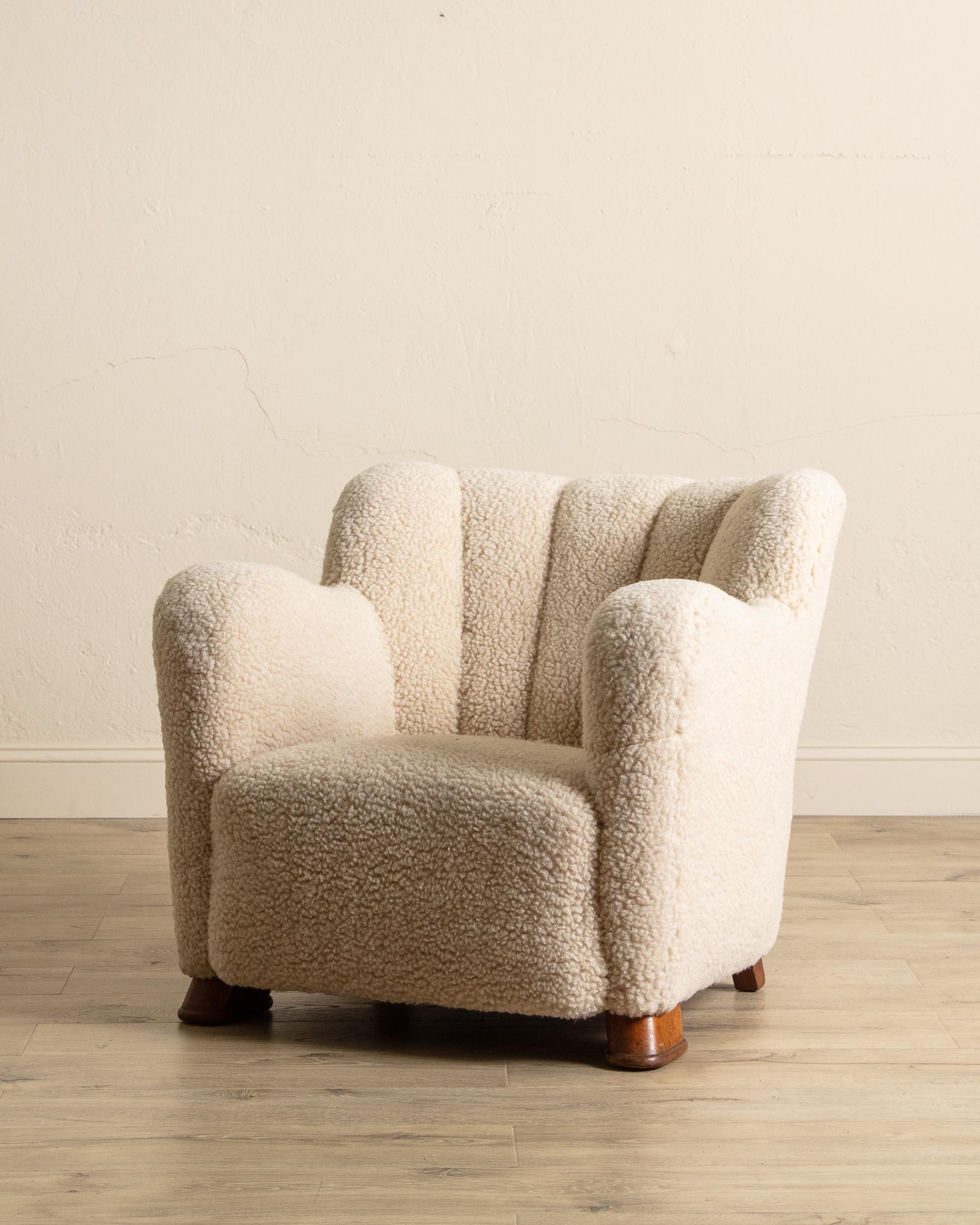This 1930s Danish easy chair, designed in the style of Flemming Lassen, exudes warmth, comfort, and timeless Scandinavian charm. Upholstered in plush lambswool, it offers an inviting texture that enhances its cozy, luxurious feel. The chair features