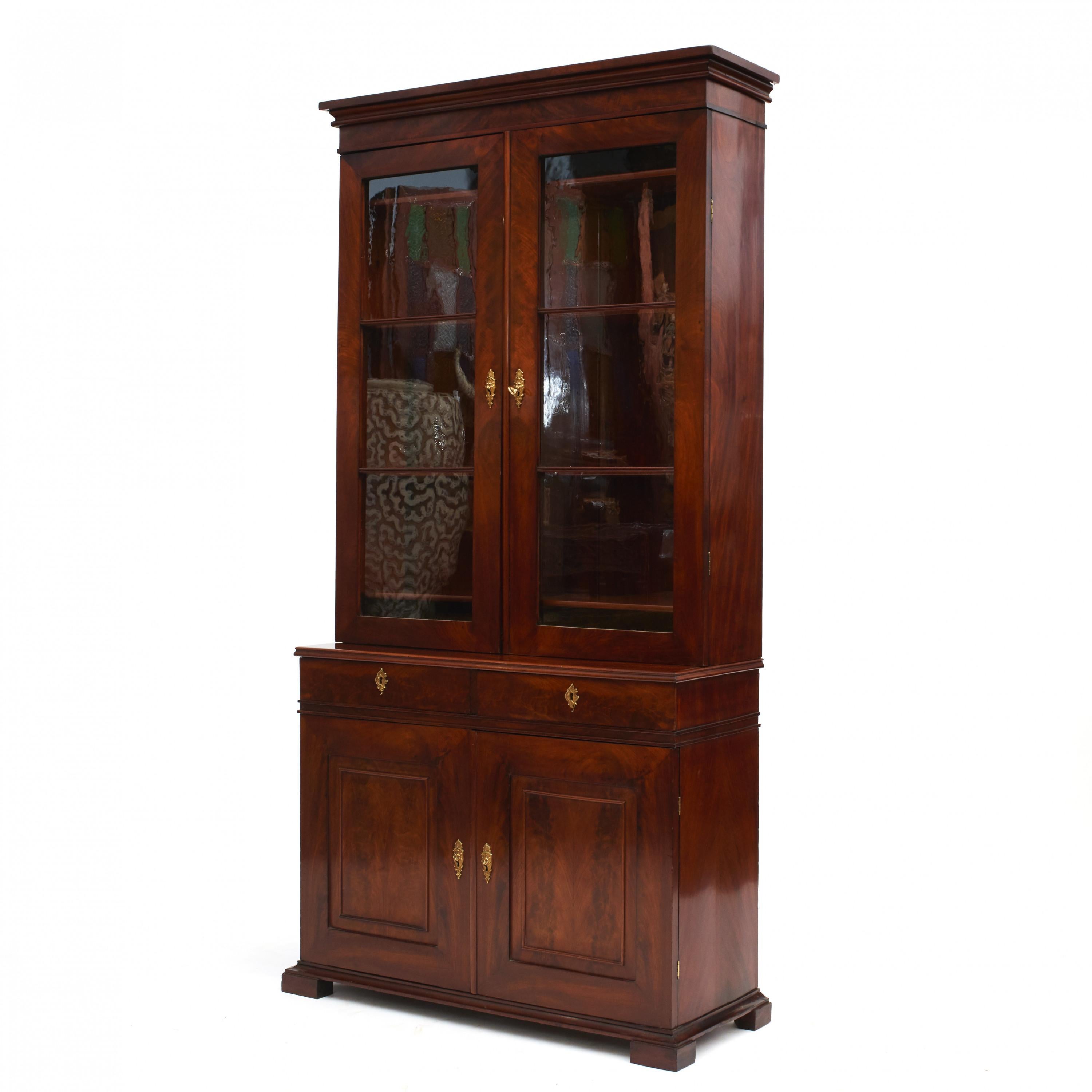 Late Empire vitrine or bookcase cabinet.
Made of radial cut mahogany with beautiful grain.
In two parts.
The upper cabinet with a pair of paned glass doors and adjustable shelving inside.
Lower section with two drawers above a pair of doors with
