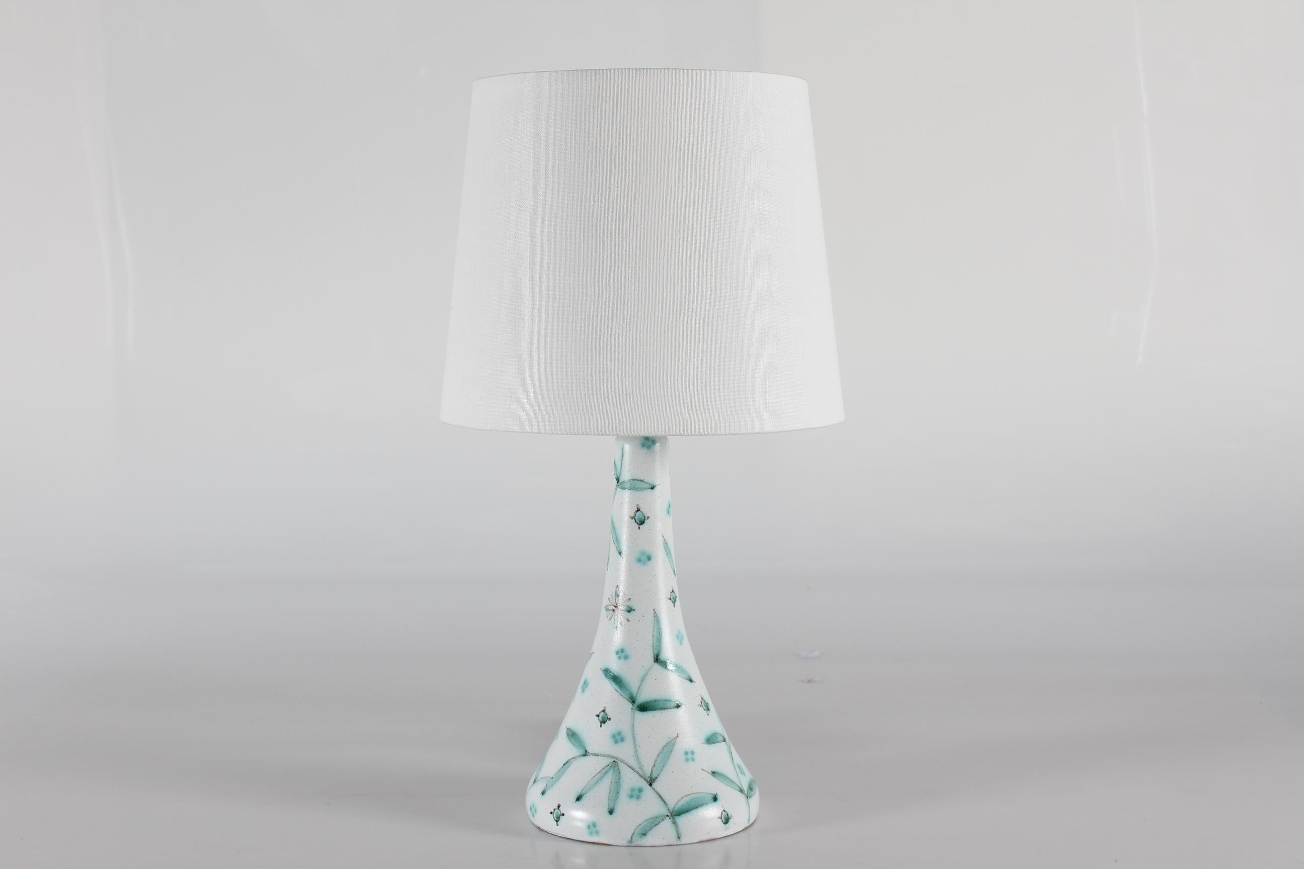 Mid-century ceramic table lamp by Danish Laurine Ceramics in Holbæk made in the 1950s.

The ceramic part is decorated by hand with a matte white base coat with pattern of slender leaves and small flower in mint green glaze.

Included is a new lamp