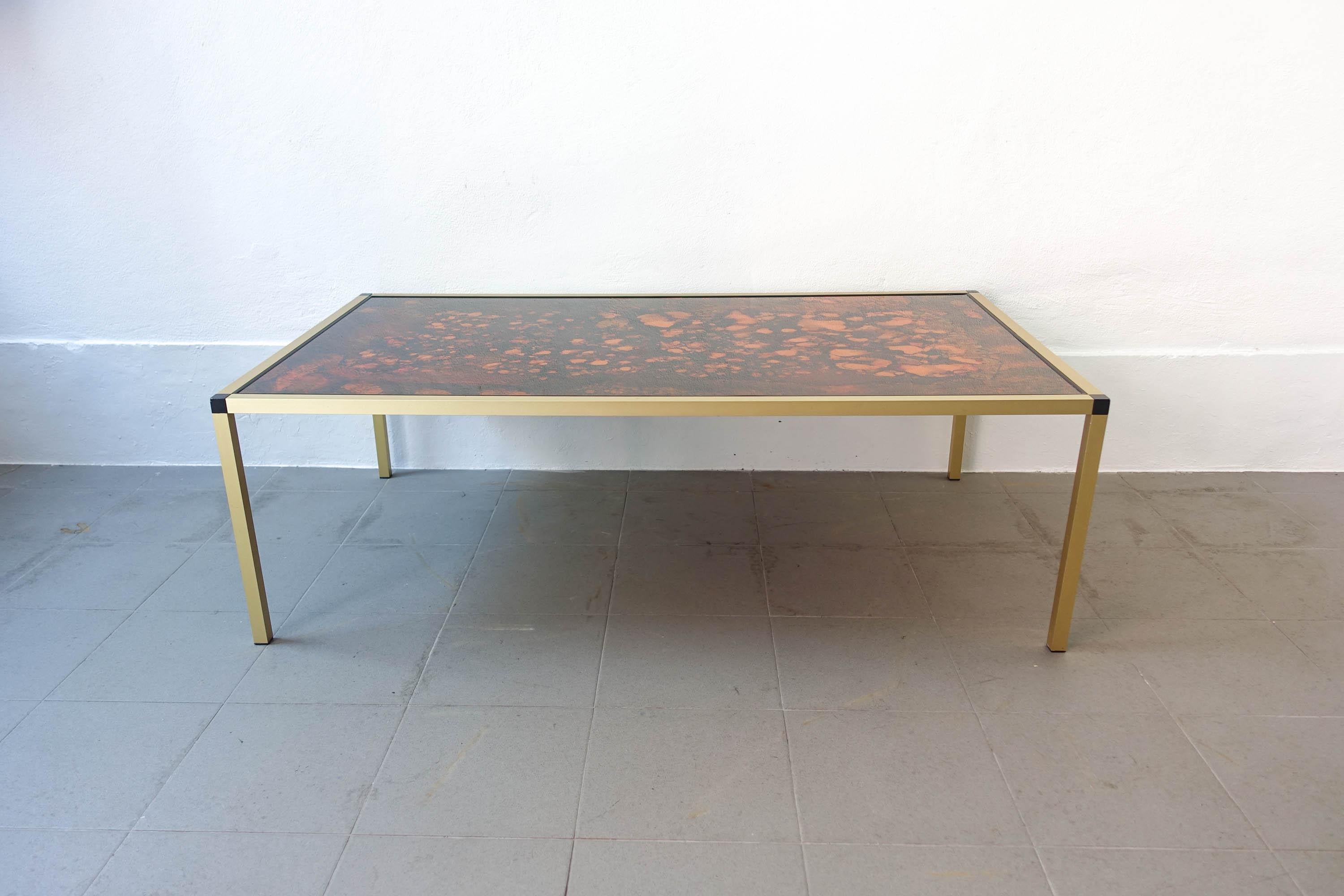 This Danish Lava pattern coffee table is made from gold aluminum with black feet and multicolored glass top. It is in a very good vintage condition.