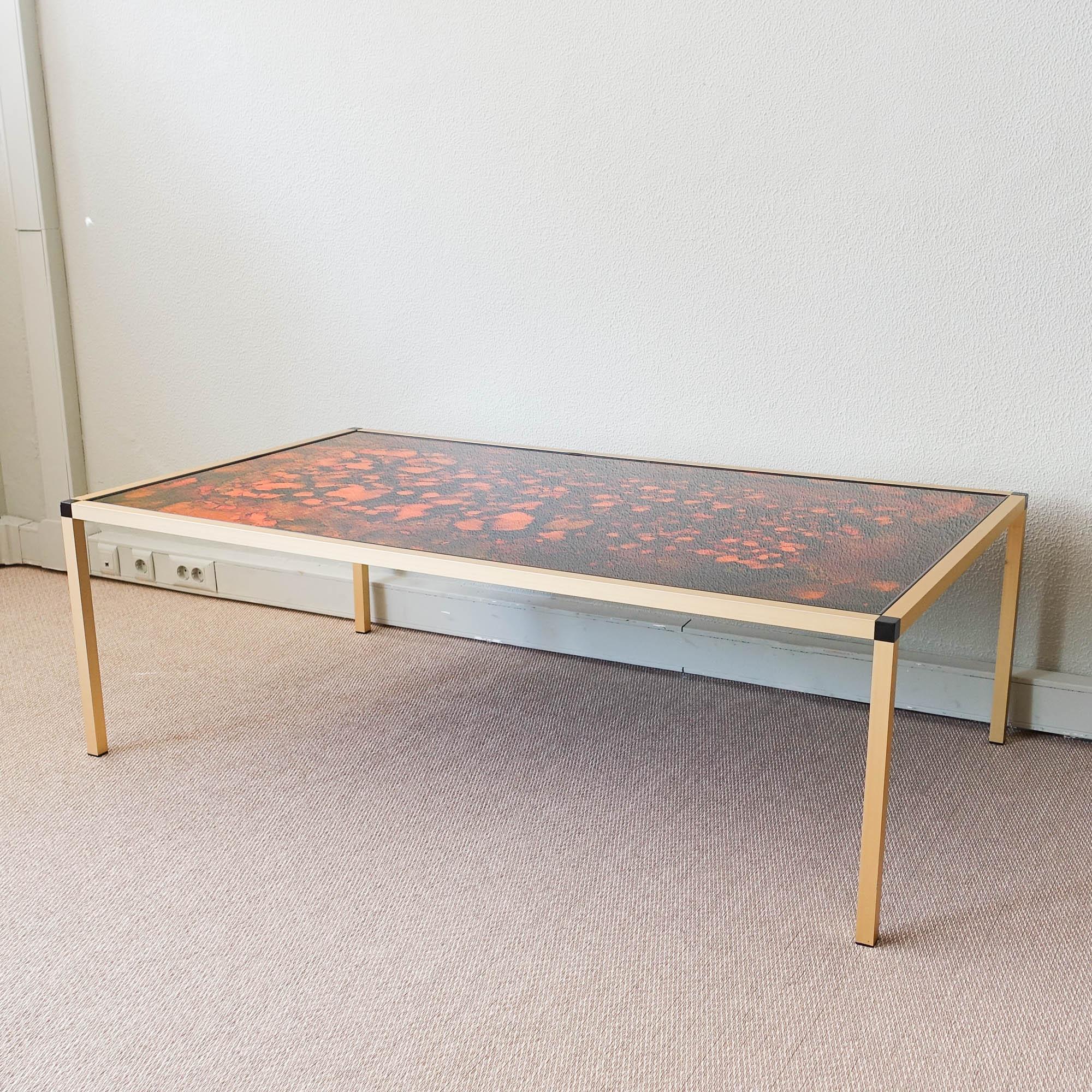 This Danish Lava pattern coffee table was designed and produced in Denmark, during the 1970's. It is made from gold aluminum with black feet and multicolored glass top. It is in a good vintage condition. 
