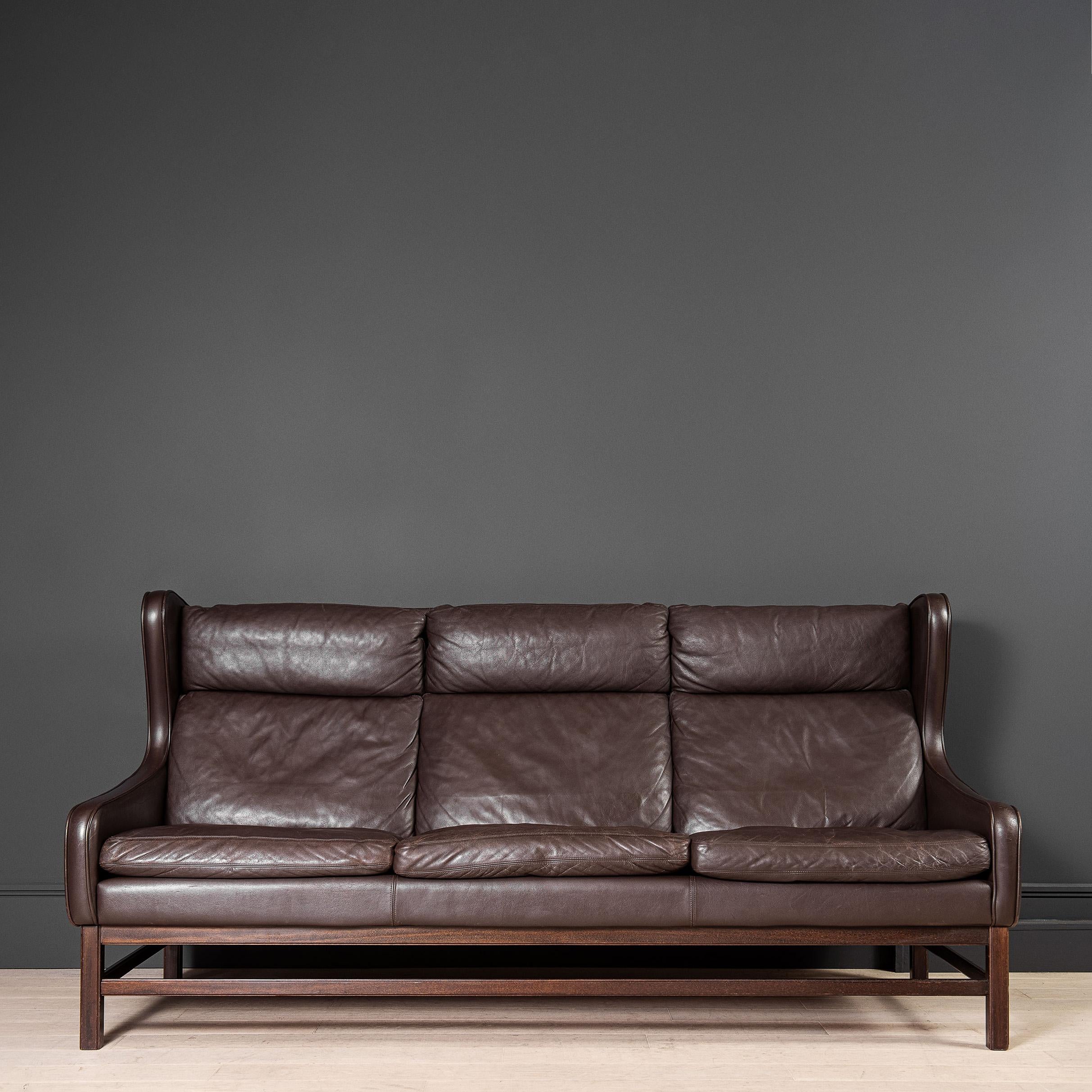 A 3 seater dark brown leather wing-back sofa. Produced in Denmark during the 1960's. This is a substantial piece and rather unusual in its design - akin to Borge Mogensen. Down filled cushions make for an extremely comfortable piece of furniture.
