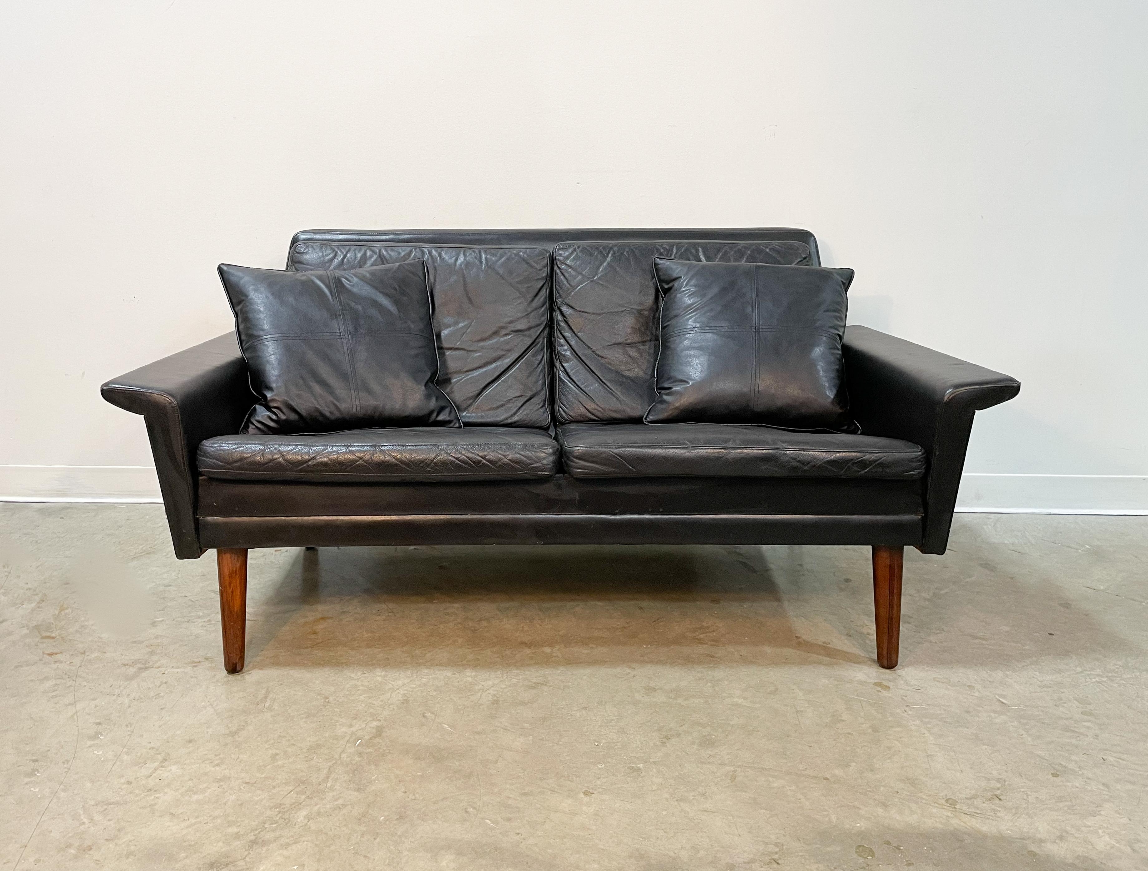 Sleek black leather Danish loveseat on Brazilian Rosewood legs from the 1960s. Very comfortable piece with a generous seat for 2-3 people. Solid oak construction with all original leather. Comfort is enhanced with two matching throw cushions