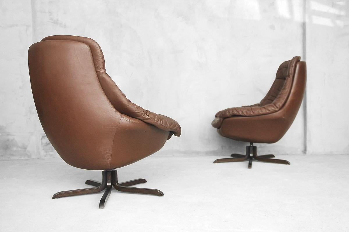 This set of two lounge chairs were designed during the 1960s by H. W. Klein for Danish company Bramin and manufactured, circa 1975. The swivel frames are made from rosewood and are upholstered in chocolate brown leather. The form in this ingeniously