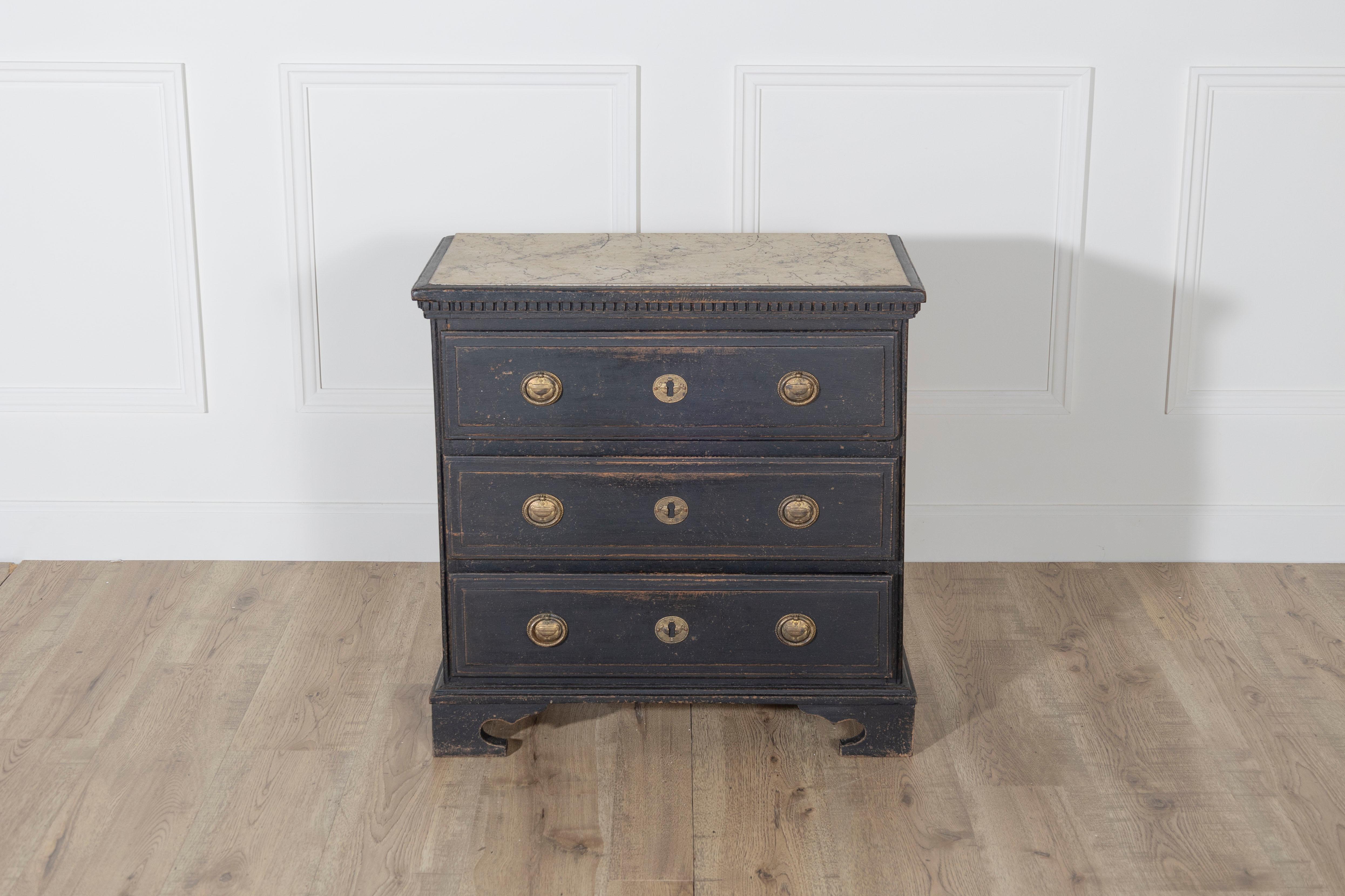A Danish chest of drawers in the Louis Seize style, crafted circa 1920 and finished in a deep black paint with charming natural patina. This elegant piece features three full-length drawers with original brass ring pulls and escutcheons, all set