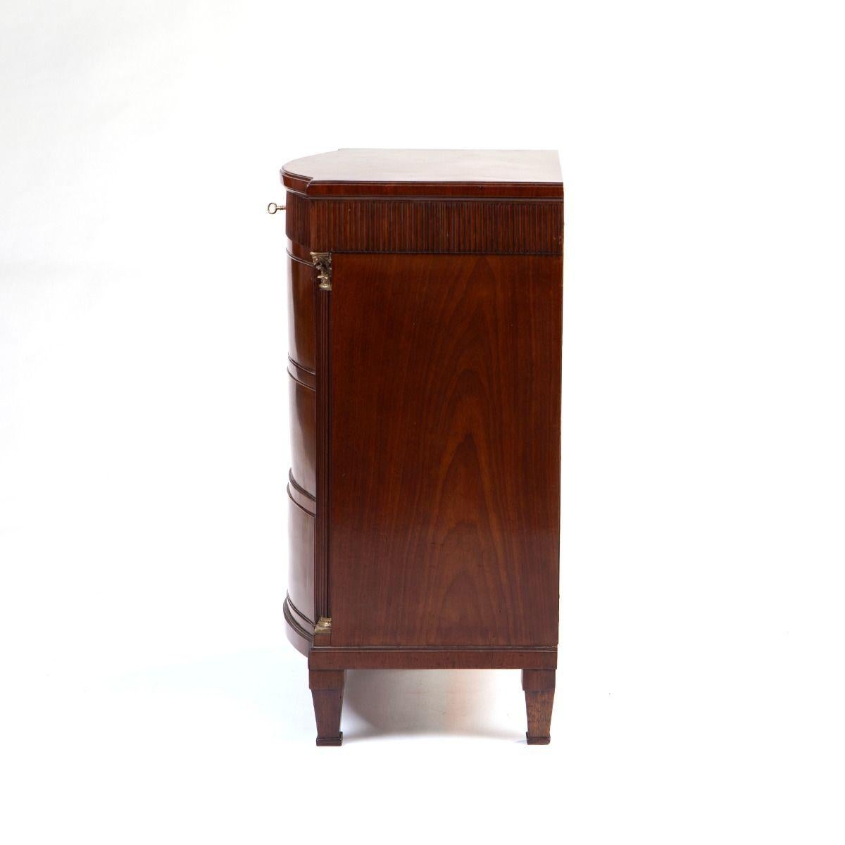An elegant Louis XVI commode crafted in rich Cuban mahogany.
The top features a moulded edge above a gently curved front with four drawers – the uppermost slightly narrower and adorned with a fluted front.
Each drawer is fitted with brass-lined