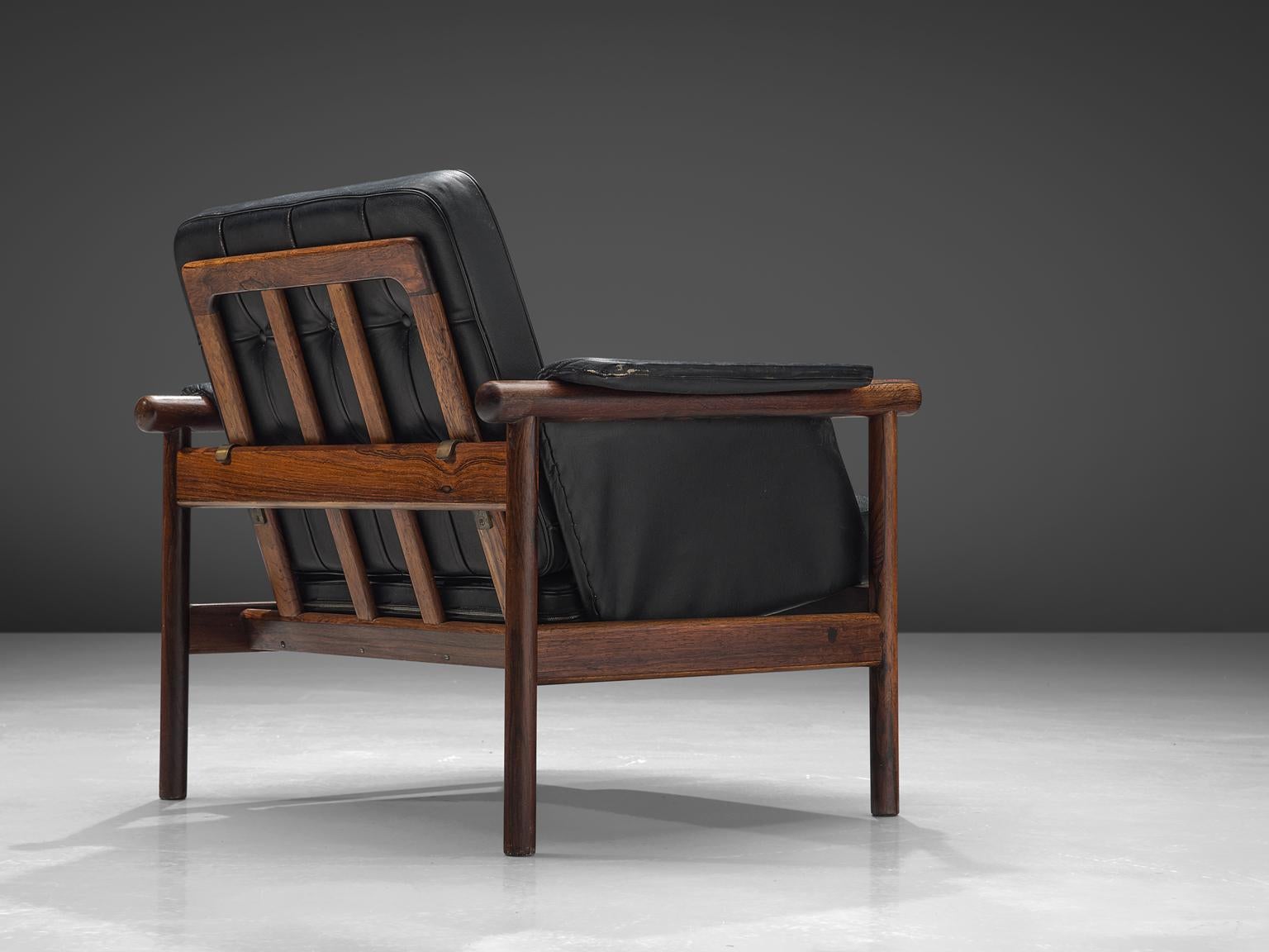 Illum Wikkelsø, easy chair, black leather and rosewood, Denmark, 1960s.

This lounge chair features a rosewood frame with slatted back and an angular, geometric frame. The tufted seat and back are comfortable and support the sitter. The backrest is