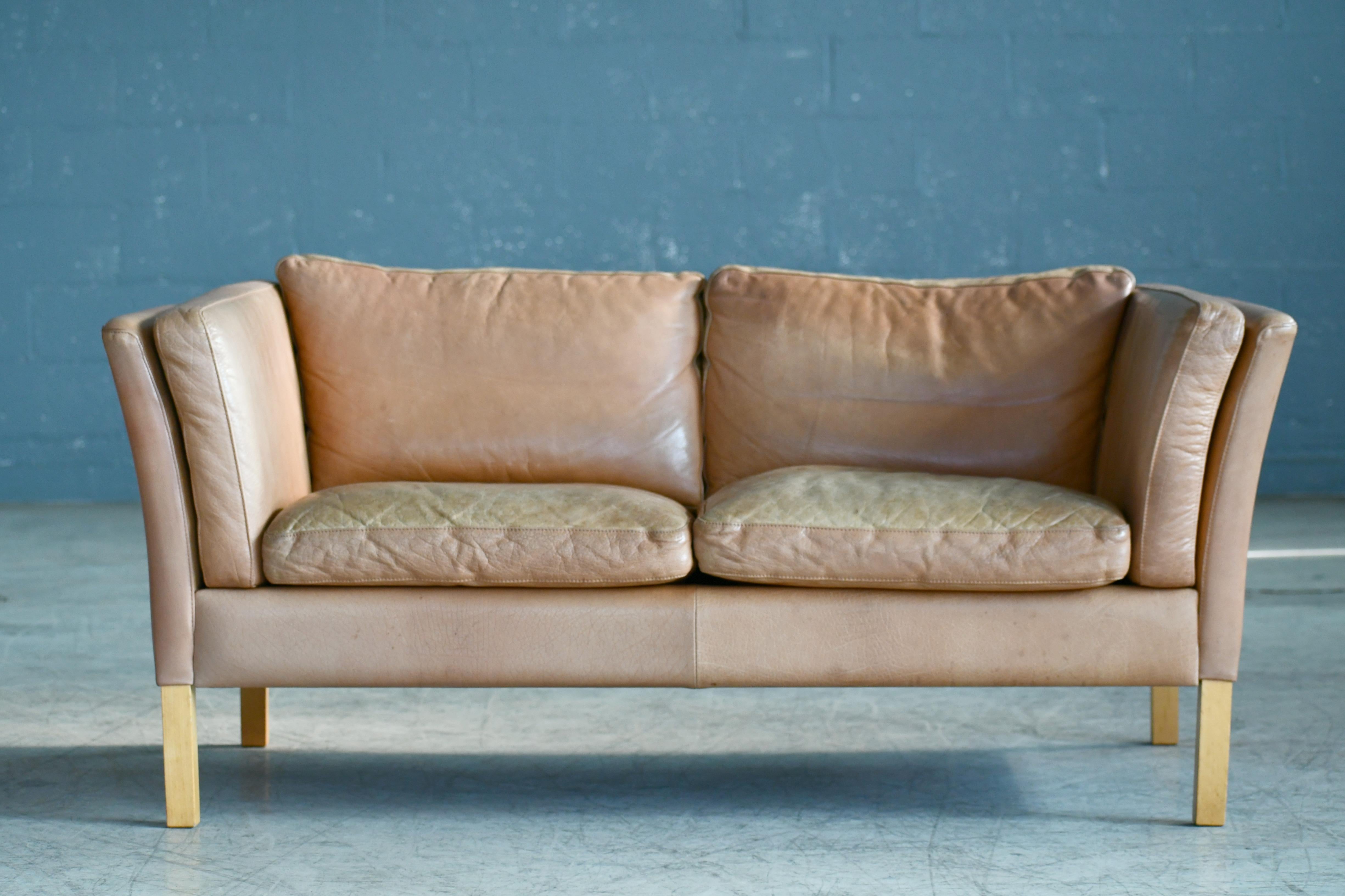 Great loveseat or two-seat sofa made by Stouby Mobler, Denmark. High quality construction in the traditional style of Børge Mogensen covered in a nice butterscotch colored leather that has faded into various shades of cream and tan colors over the
