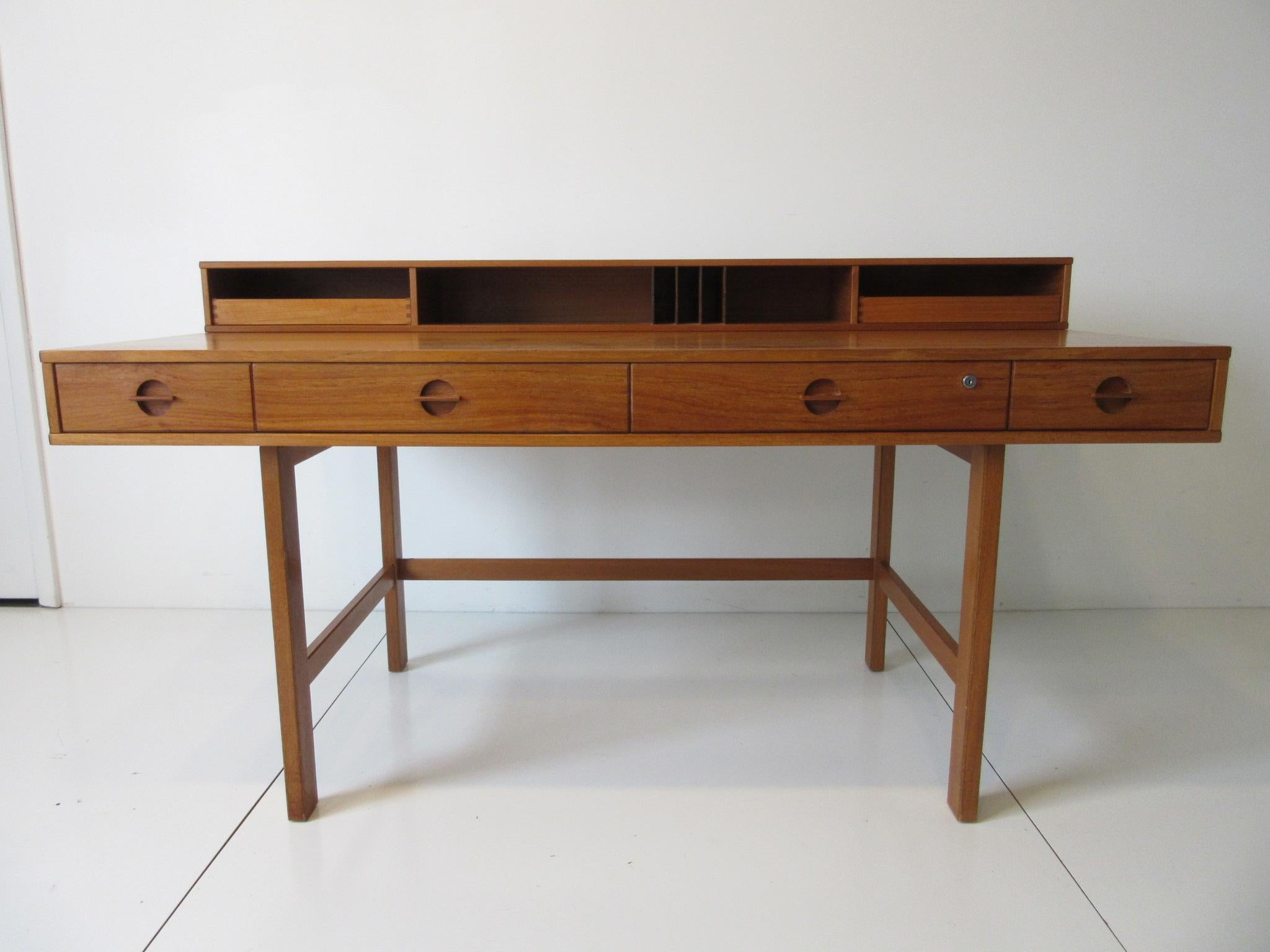 A wonderful well designed and Classic teak flip top desk with four front drawers having built in matching pulls, two upper slide out storage drawers, letter compartment and bins. The back side has three open storage bins and when the back side is