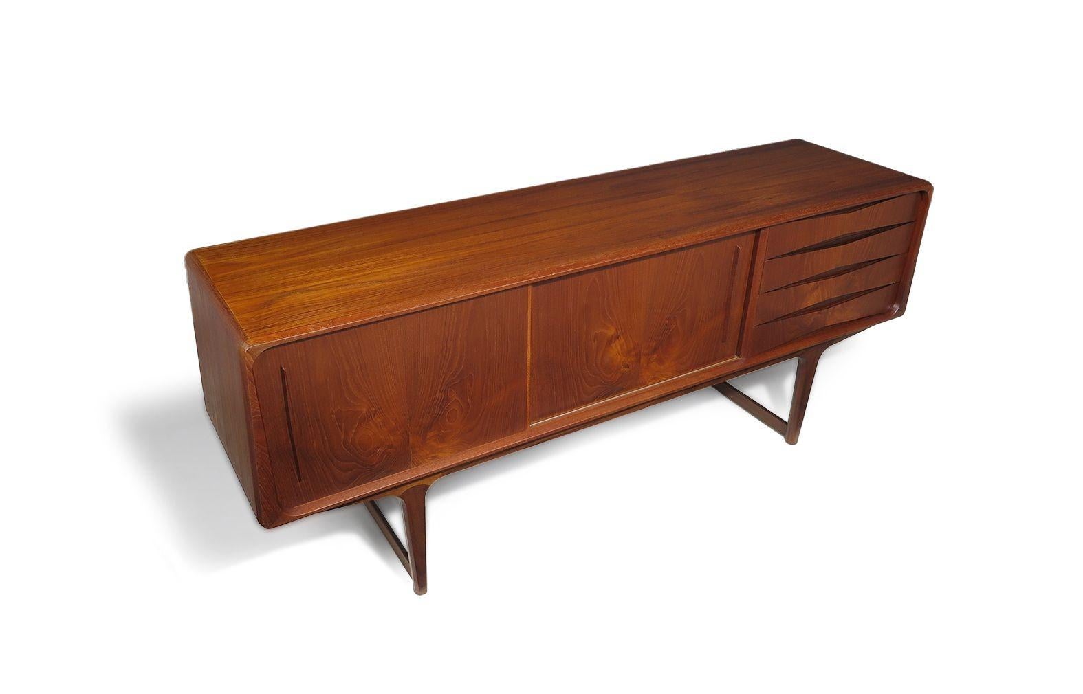 Danish Credenza with unique angled sides, handcrafted from old-growth teak features four drawers with recessed pulls and two sliding cabinet doors with wide book-matched grain, opening to reveal a teak interior with adjustable shelves. This