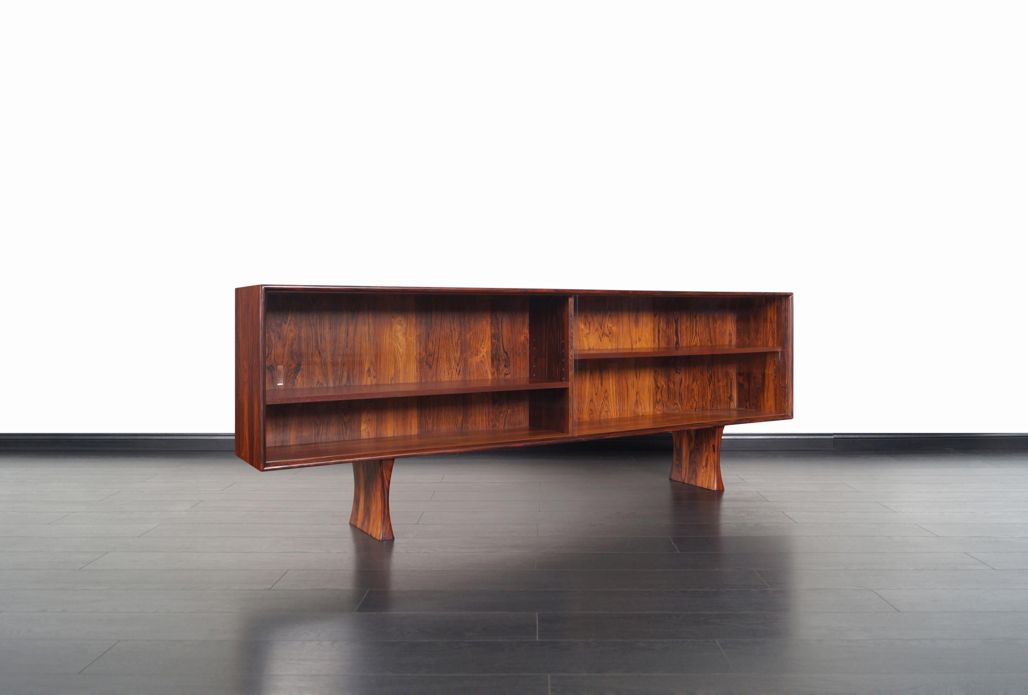 Danish modern Brazilian rosewood bookcase or credenza designed by Bernhard Pederson & Son. This low profile bookcase features two sliding glass doors that smoothly opens to reveal two adjustable shelves. The case sits on two solid rosewood pedestal