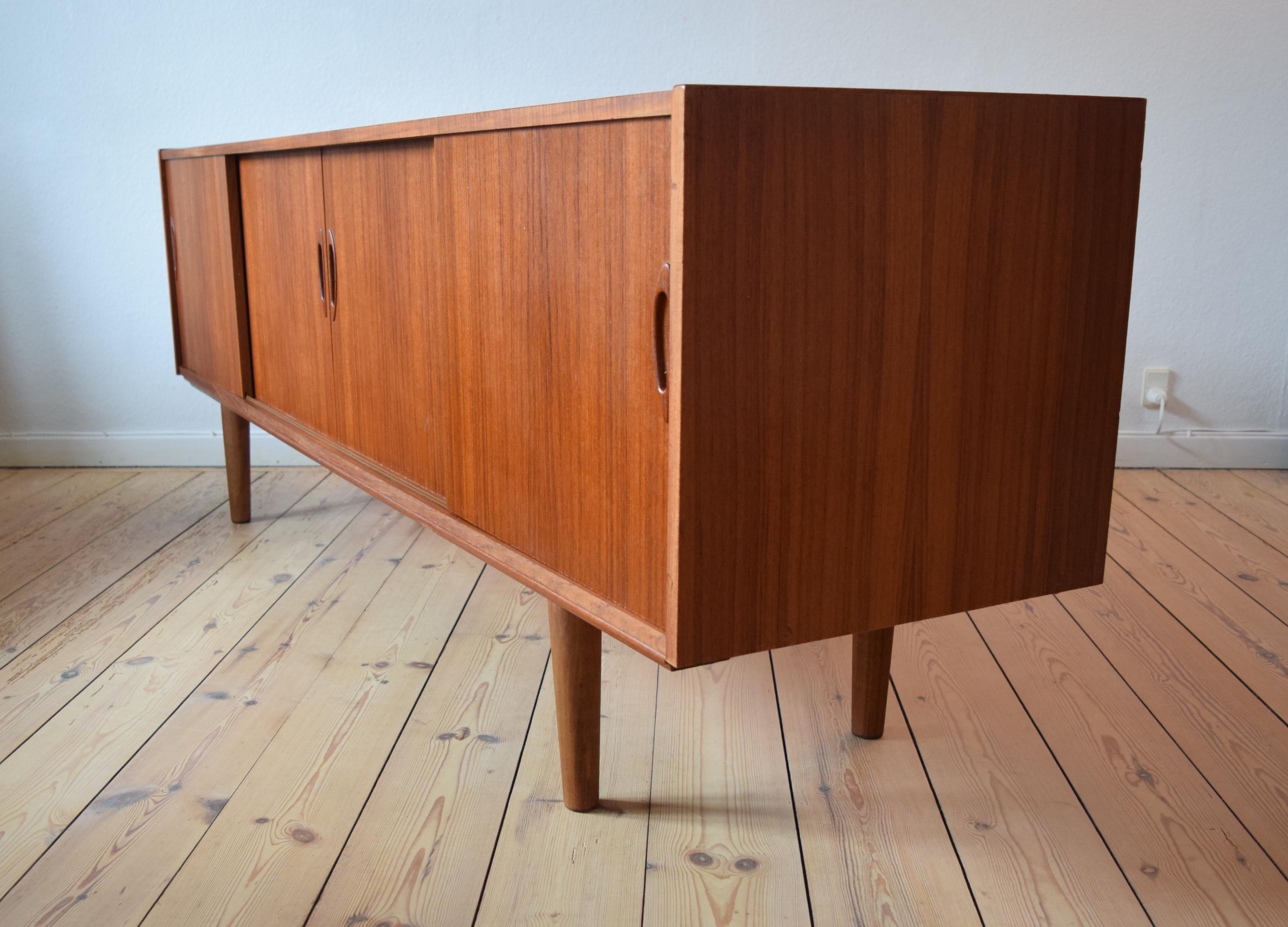 Midcentury sideboard, manufactured in Denmark in the 1960s. This piece features four sliding doors with interior compartments. Bar section, shelf and three drawers. Sits on turned and tapered teak legs. It is rare to find these sideboards with such