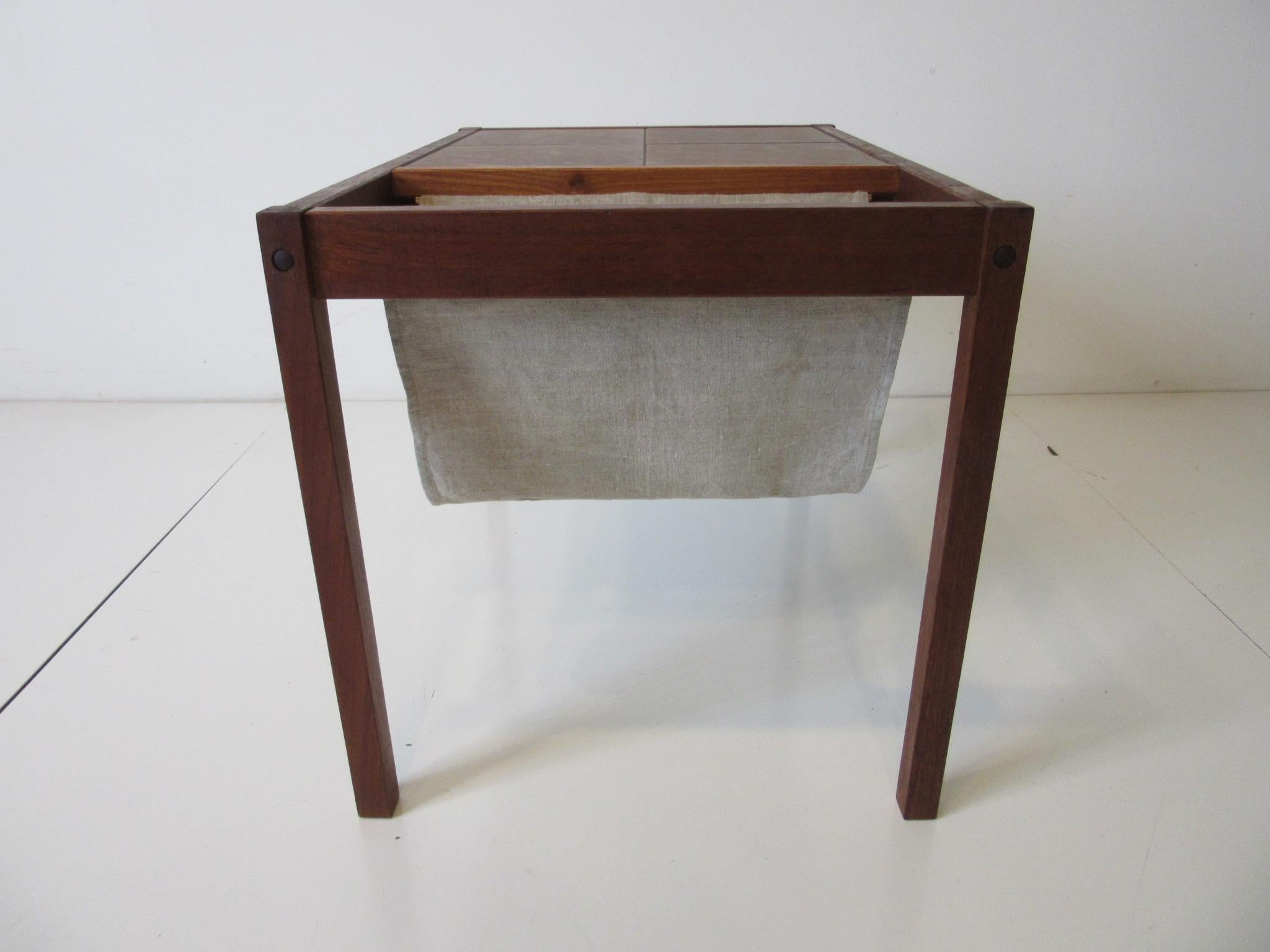 A dark teak wood framed magazine rack with hanging fabric sling the other end of the top having four large glazed pottery tiles. Retains the ink stamp of origin made in Denmark in the manner of BRDRK Furbo.