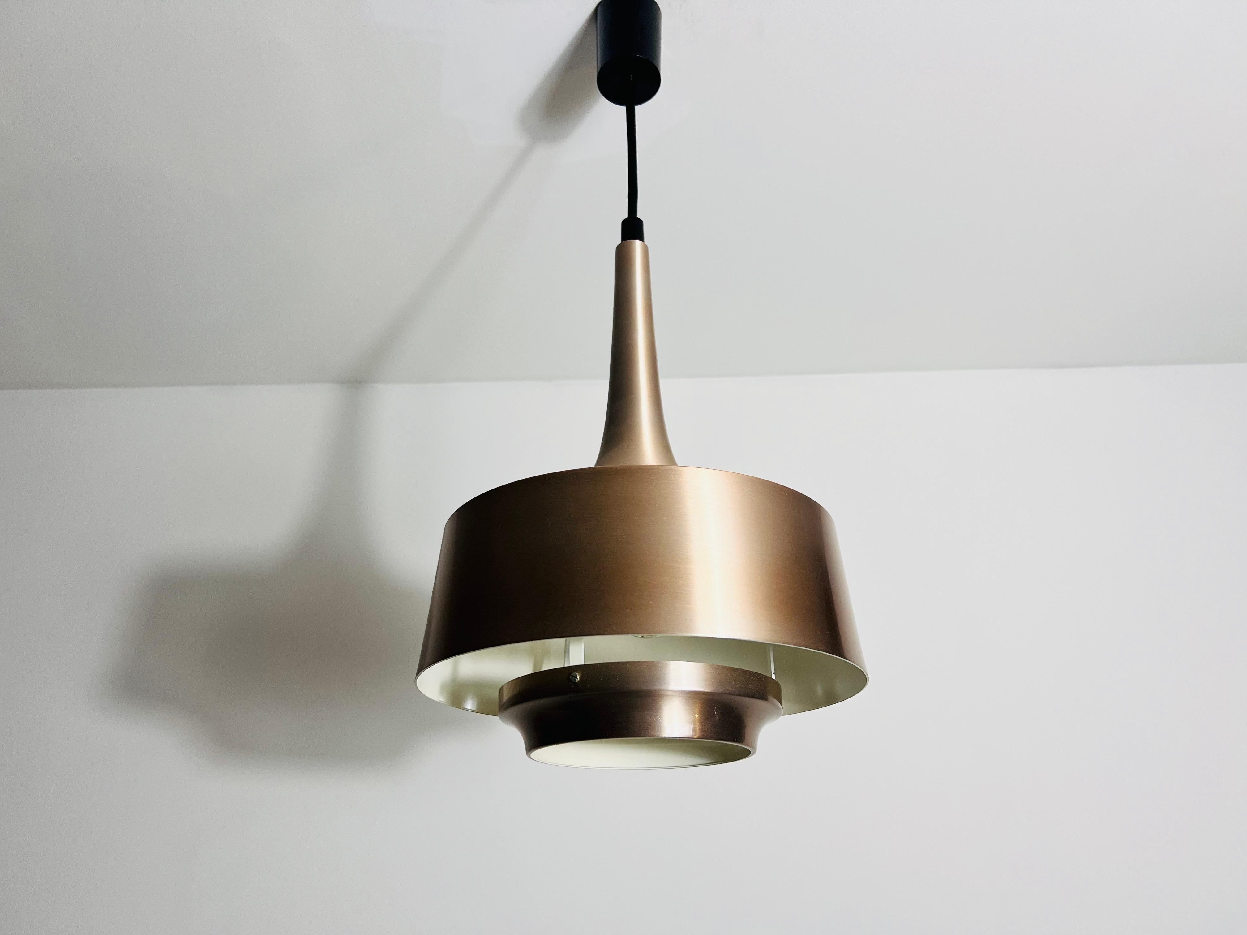 Lampada a sospensione danese in metallo degli anni '80 con una sorprendente finitura esterna color rame. Questo elegante apparecchio emette una luce calda e invitante, che lo rende un'ottima aggiunta a diversi spazi interni. La lampada è realizzata