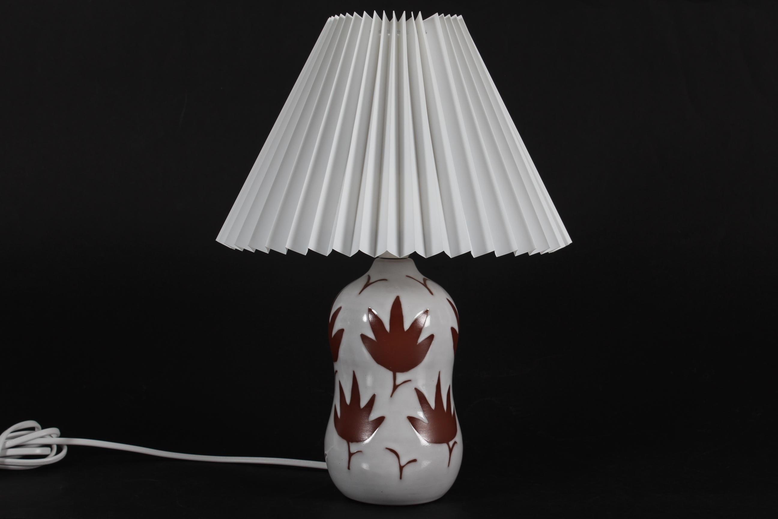 Danish table lamp made designed and made in the 1950s

The ceramic lamp base has a leaf pattern that emerges in the contrast between a unglased part and a part with white glaze. 

Included is a new clip on pleated lampshade designed and made in