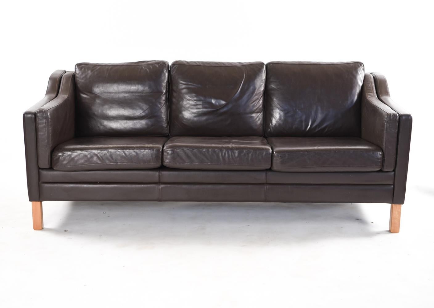 A Danish midcentury three-seat sofa in the manner of designer Børge Mogensen. Upholstered in rich, chocolate brown leather, this sofa displays an attractive patina only possible from genuine age. A timeless, sought after Scandinavian Modern design.
