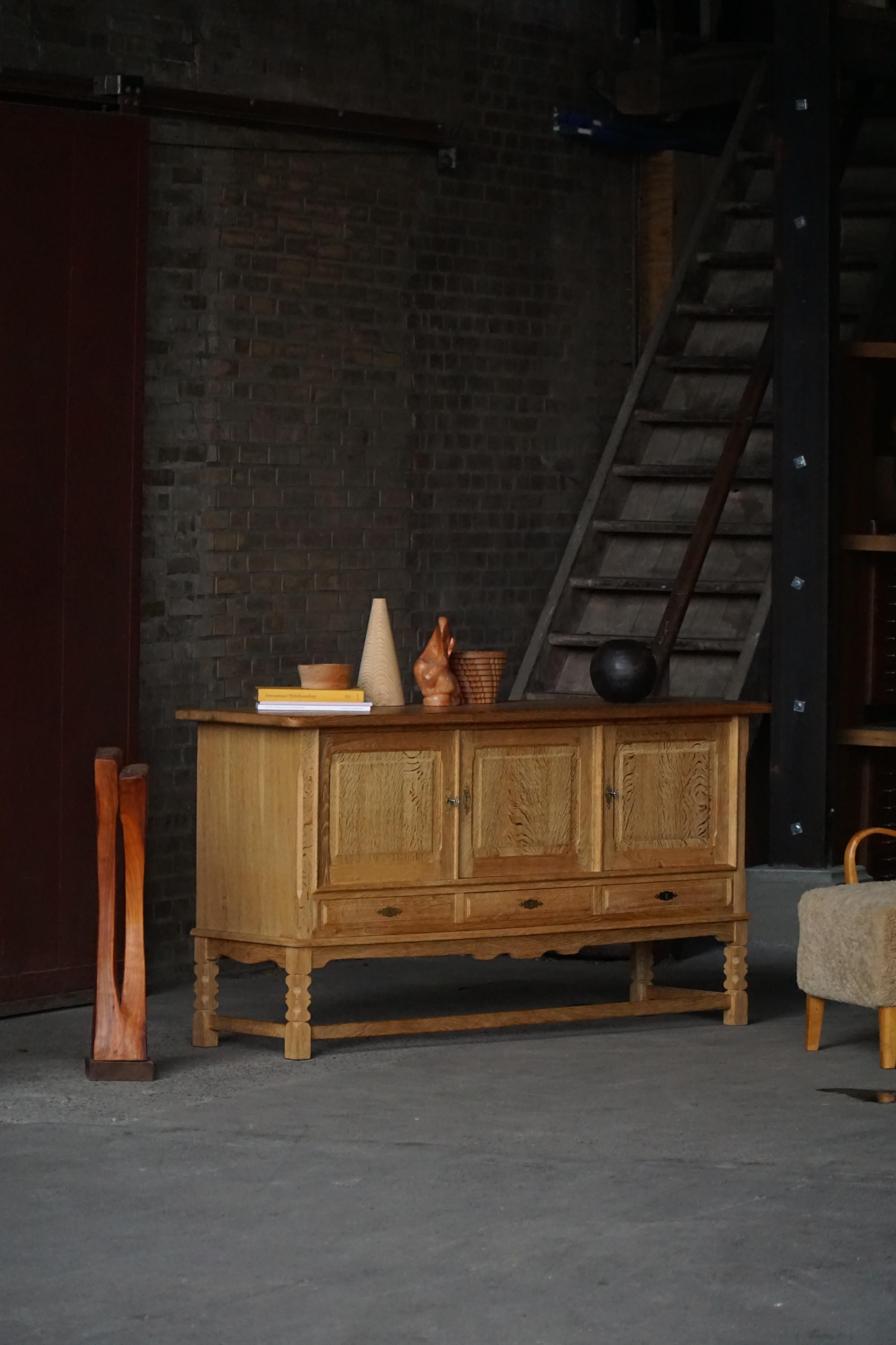 Un élégant buffet en chêne de Henning Kjærnulf, fabriqué au Danemark vers les années 1970. La pièce présente une forme architecturale épurée reposant sur un socle, soulignant sa présence sculpturale et ses proportions raffinées.

La façade comprend