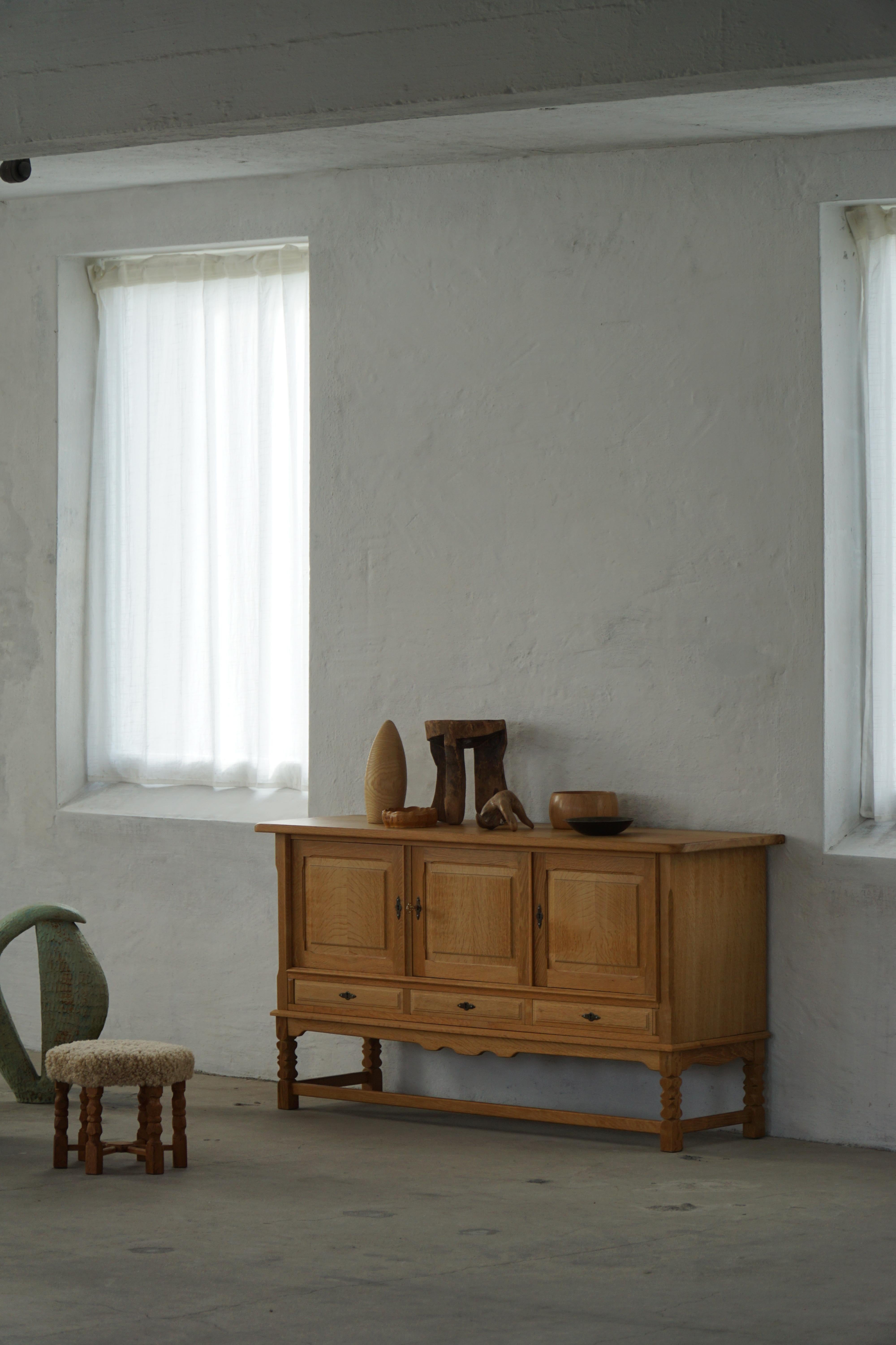 Un élégant buffet en chêne de Henning Kjærnulf, fabriqué au Danemark vers les années 1970. La pièce présente une forme architecturale épurée reposant sur un socle, soulignant sa présence sculpturale et ses proportions raffinées.

La façade comprend