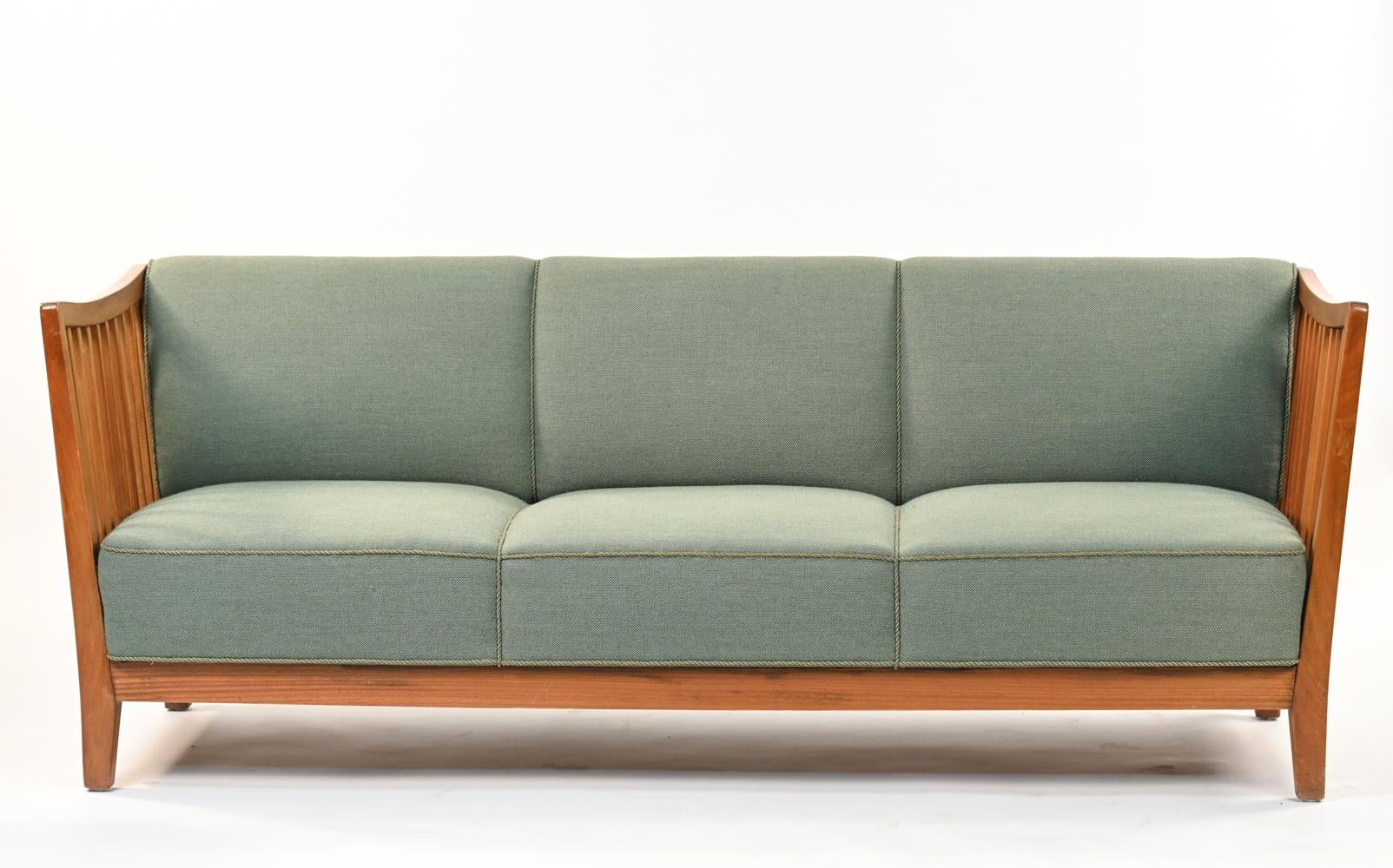 A Danish mid-century three-seater sofa in the manner of designer Carl Malmsten. Featuring jade green wool upholstery with piped trim, with Danish upholstery label underneath. The mahogany frame features squared spindle sides.
