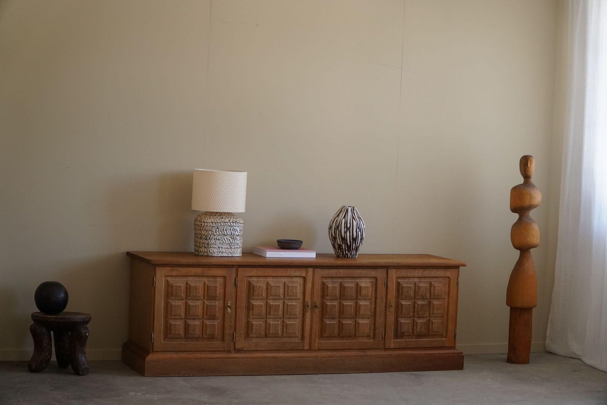 A spectacular low brutalist sideboard in oak and with brass fittings. Made by a Danish cabinetmaker in the 1950s. This piece is in a good vintage condition, with highlighted details such as the sculptural front design. 

This object will fit into