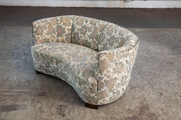 Viggo Boesen style banana shaped or curved Loveseat made in Denmark, circa 1940. This small sofa will make a strong statement in any room. Beautiful round voluptuous lines and with large block legs. Re-upholstered at a later pont in a floral cotton