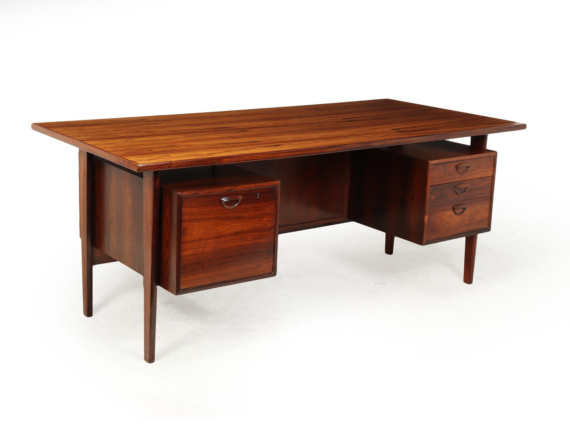 A mid century floating top rosewood desk model FM59 designed by Kai Kristiansen and produced in Denmark by Feldballes Møbelfabrik of good proportions with three drawers to the right and a filing drawer to the left and two lockable cupboards to the