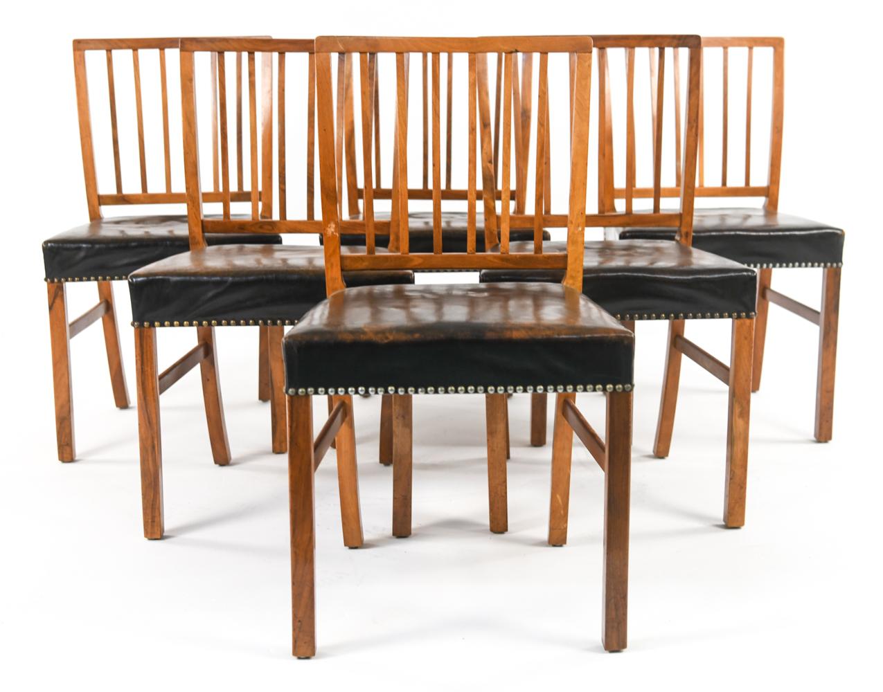 A handsome Danish mid-century mahogany dining suite comprised of (6) dining chairs featuring elegant brass nailhead trim to brown leather patinated seat upholstery and slatted backrests, and a round dining table with (4) 23.5