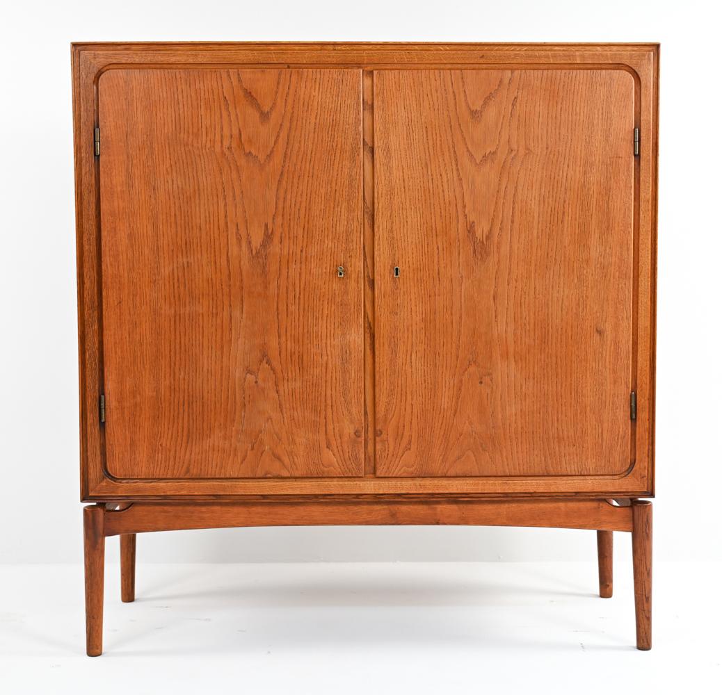 A handsome Danish mid-century tall wardrobe cabinet in fine oak wood. Two cabinet doors, with a functional locking mechanism and key, open to reveal a fitted interior with adjustable height shelving on one side and pull-out open drawers on the