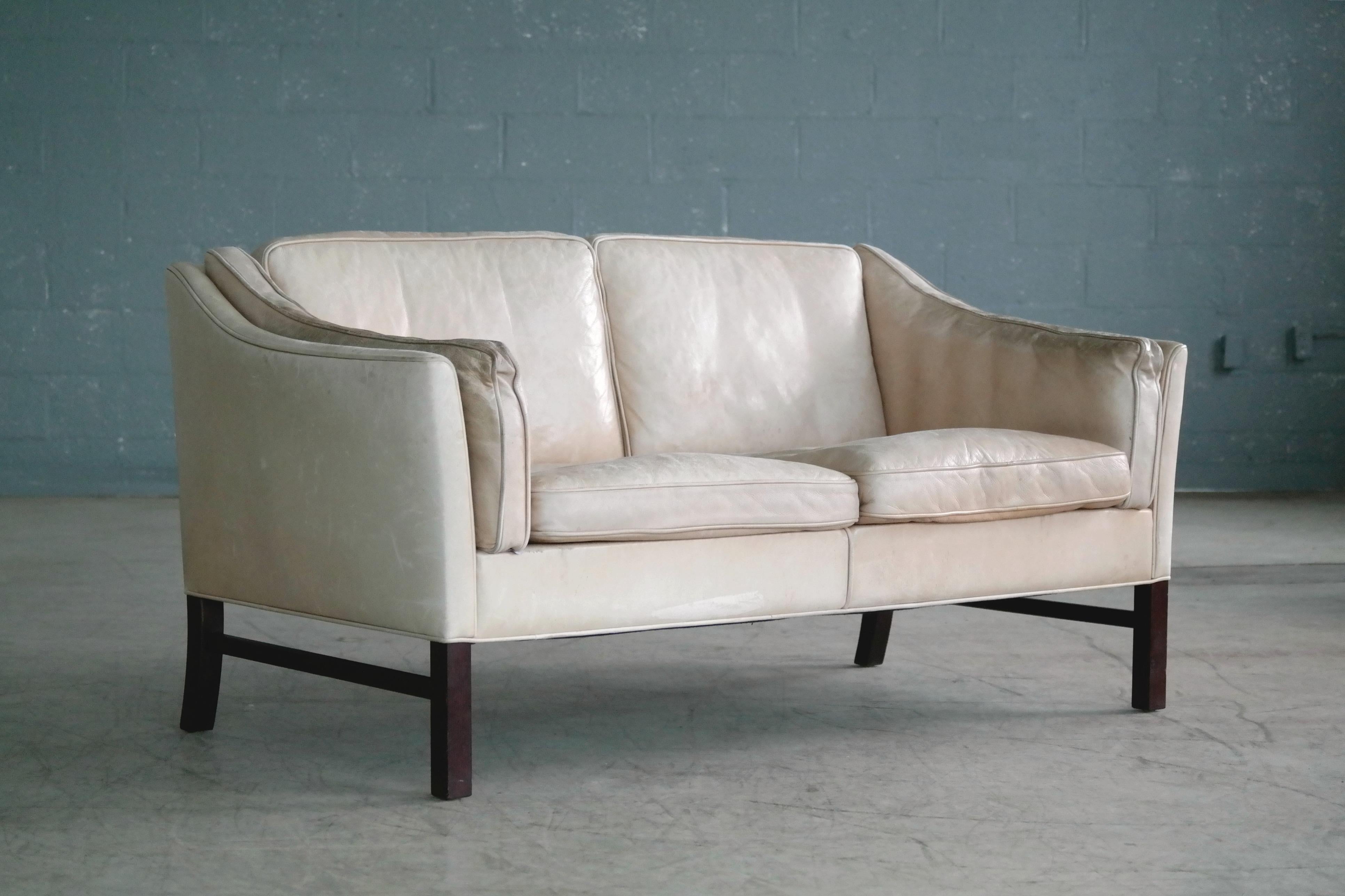 Great loveseat or two-seat sofa attributed to Illum Wikkelso made by Grandt Mobler of Denmark sometime in the 1970s. High quality construction with a slightly scalloped back with semi-down filled cushions covered in a nice tan top grain leather that