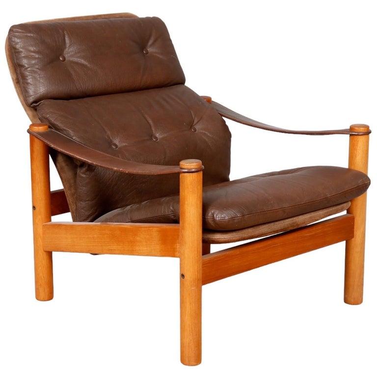 A Danish mid-century teak lounge chair dating from the 1970’s. Upholstered in beige linen and suede, with loose button tufted brown leather cushions and matching brown leather strap arms.
