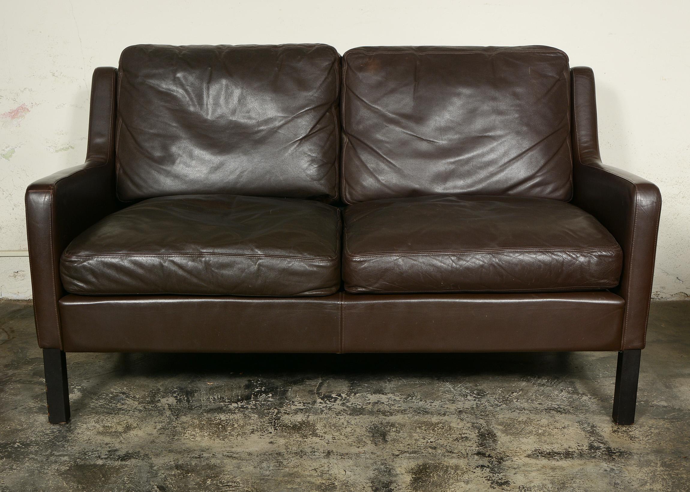 This two seat Danish sofa is covered in a dark brown leather. The styling is reminiscent of Kaare Klint or Borge Mogensen. The leather shows a little rubbing and wear in spots.