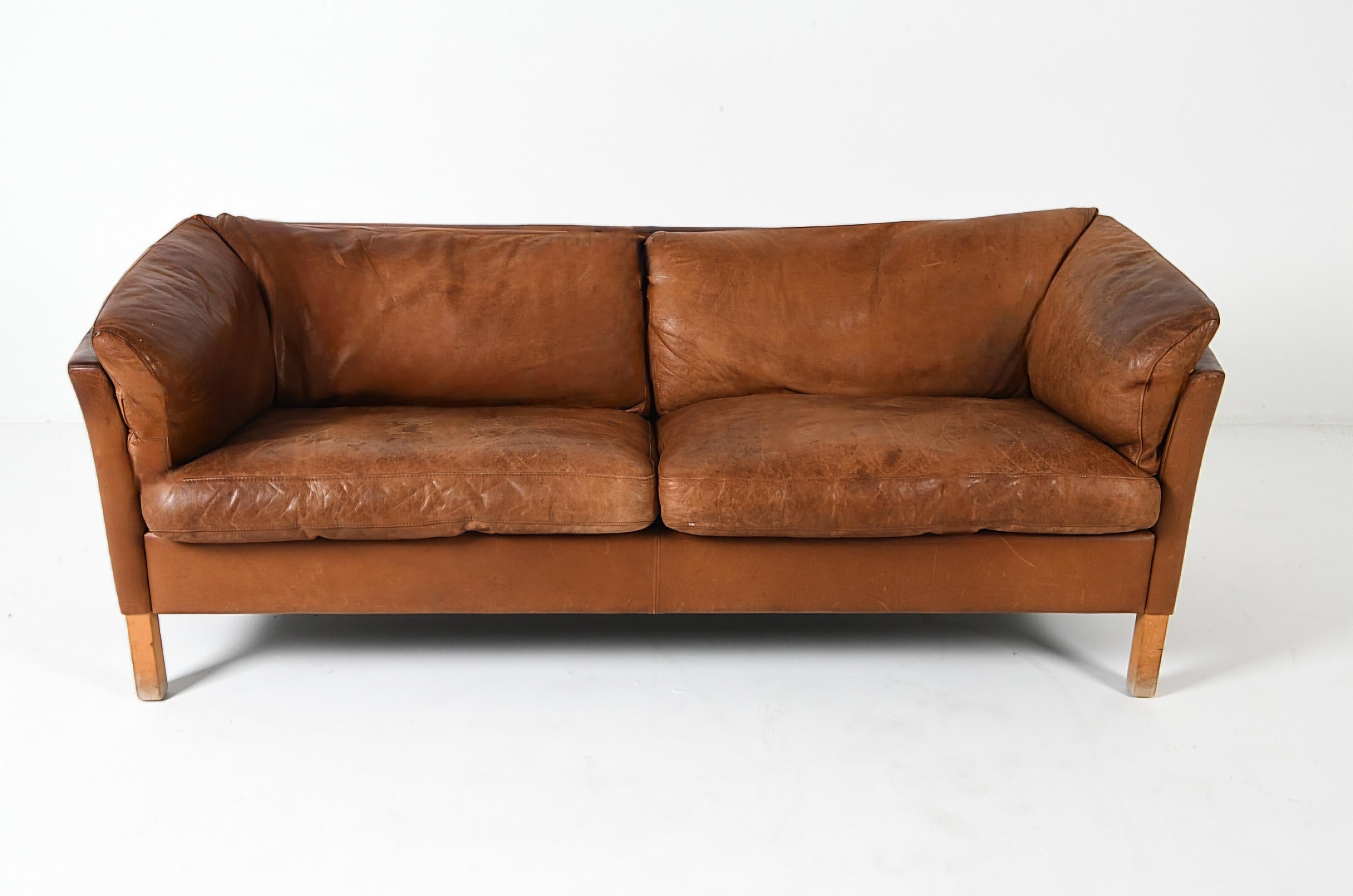 Luxueux canapé en cuir de Mogens Hansen. Ce canapé se caractérise par des accoudoirs à rail légèrement incurvés et des silhouettes douces et raffinées. Il est réalisé en cuir souple, avec une patine douce et délavée par le soleil que seules les