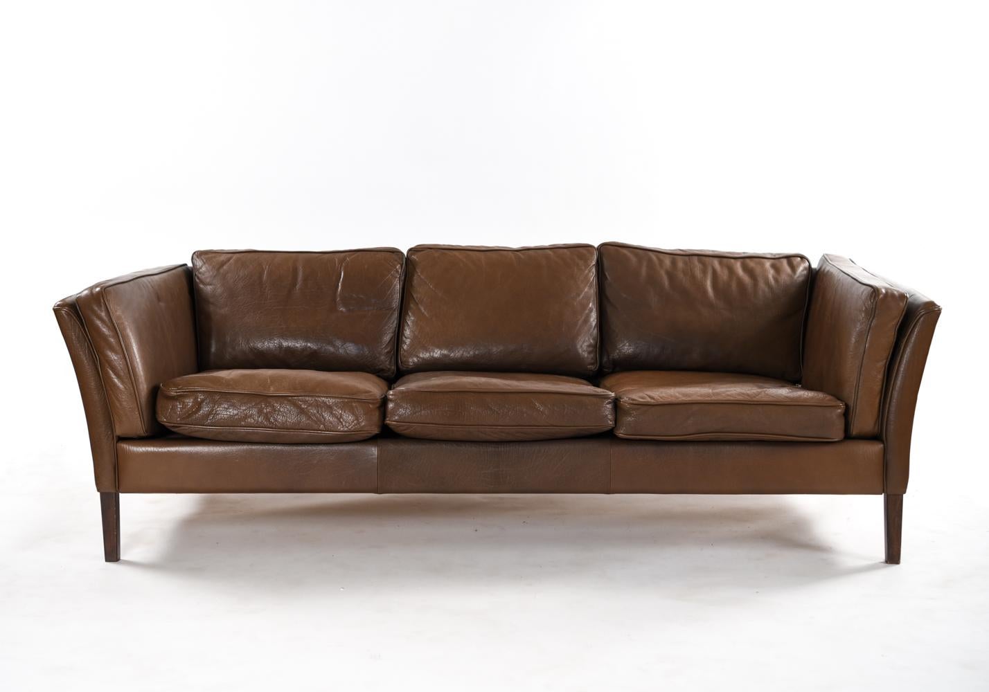 A Danish midcentury sofa that can seat three comfortably, upholstered in vintage brown leather with a lovely patination. This piece by Mogens Hansen shows clean, modern lines characteristic of Danish design.